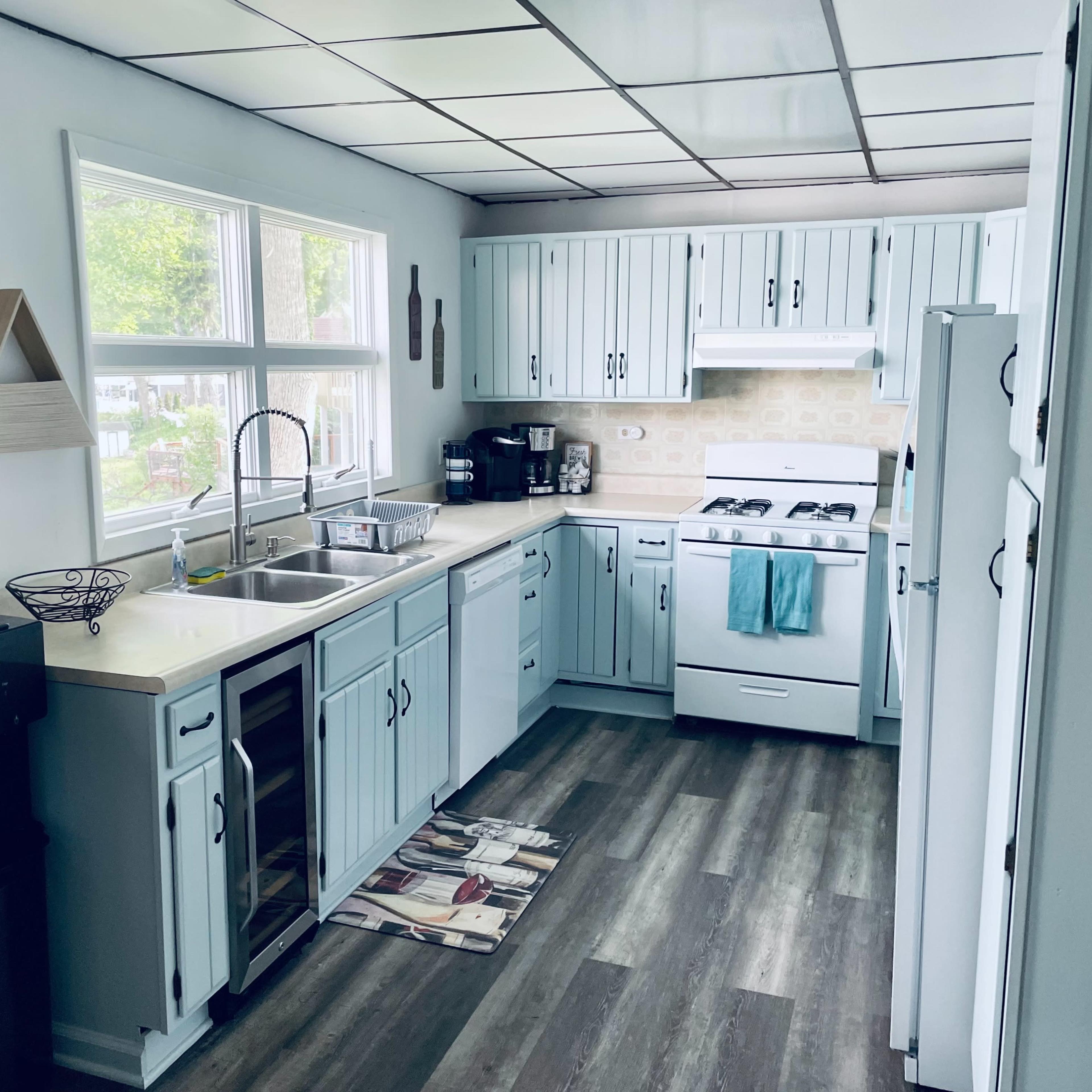A kitchen with light blue cabinets, a sink, a stove, and a refrigerator, featuring a small dining mat on the floor.