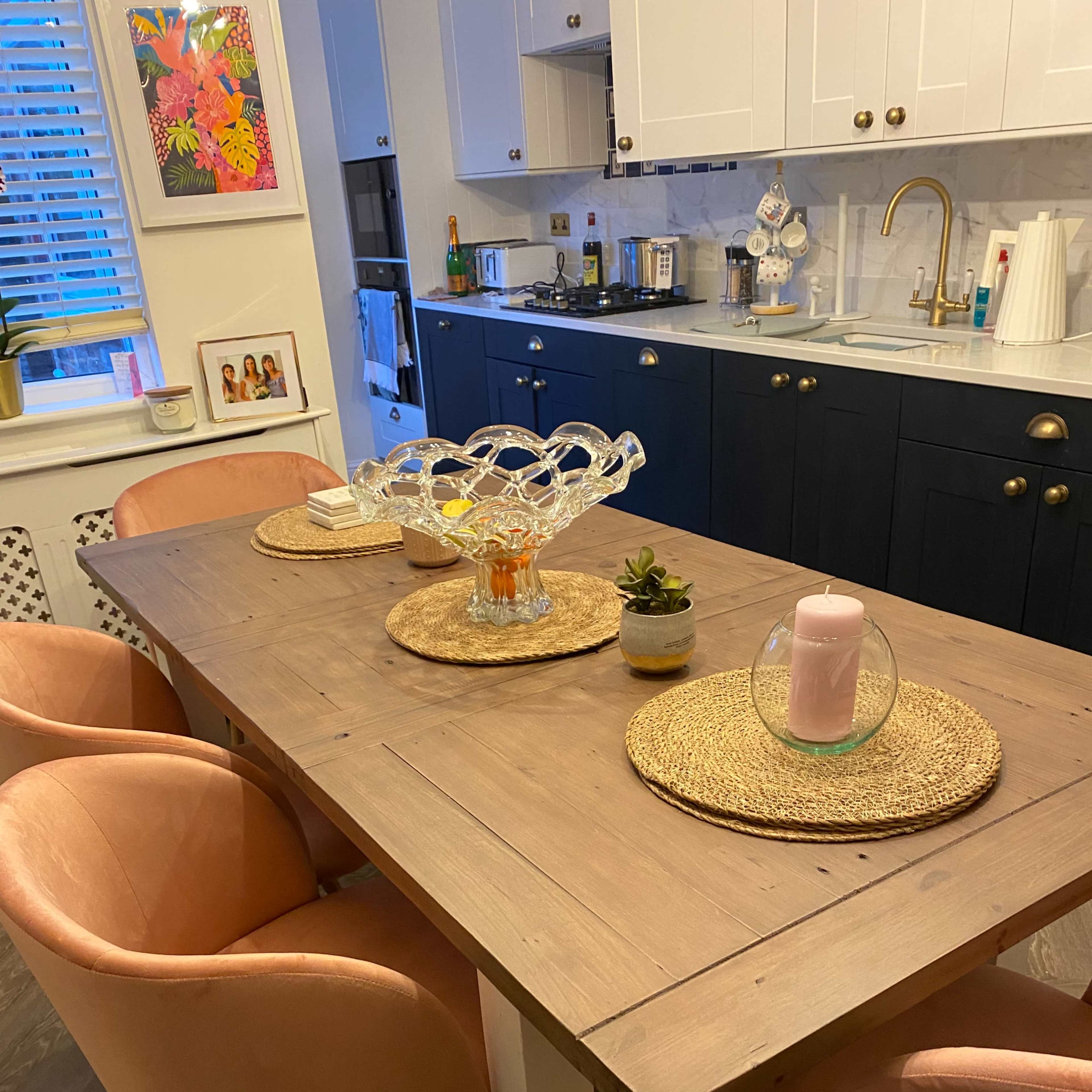 A wooden dining table is set with round placemats, decorative glassware, and chairs with pink upholstery in a modern kitchen.