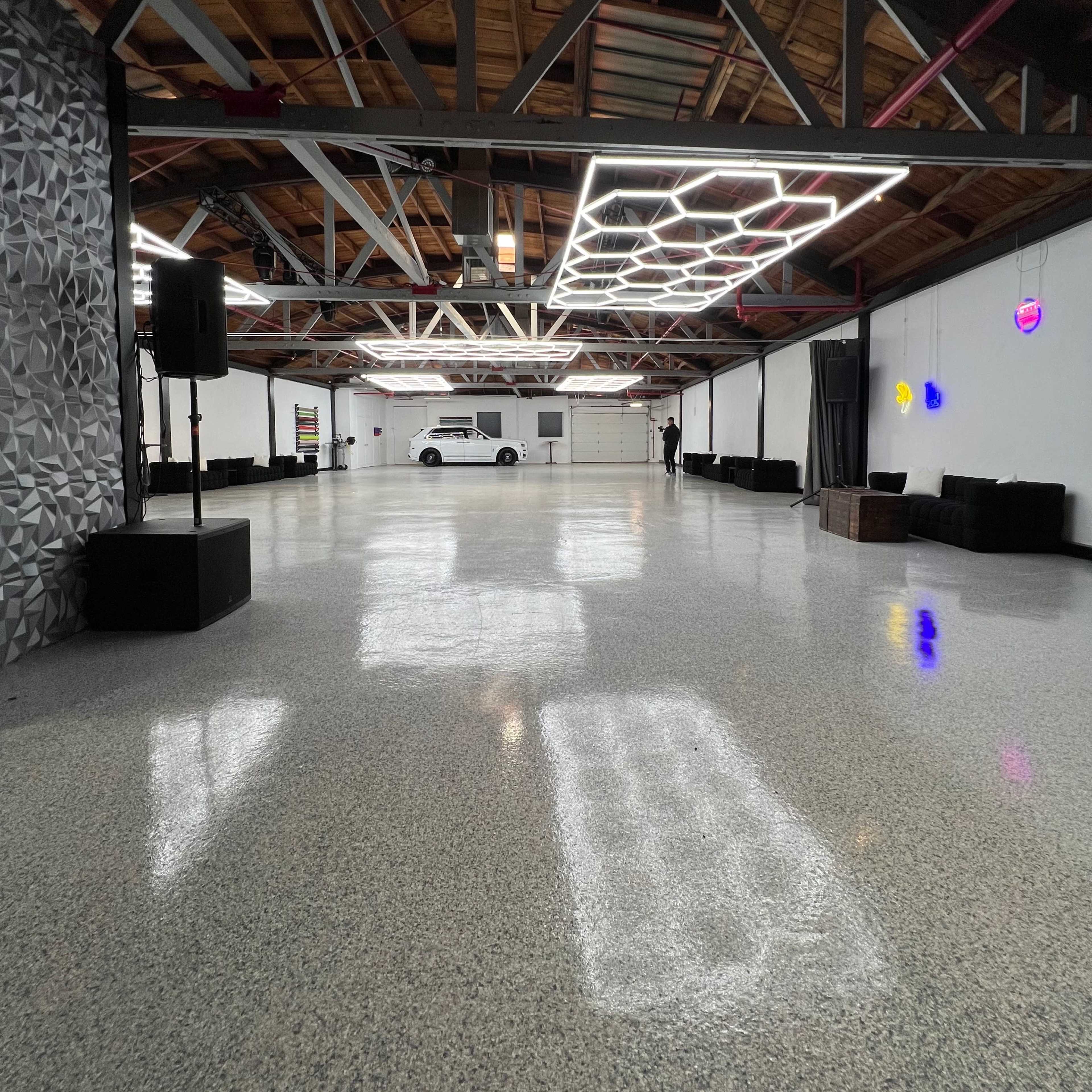 A spacious, modern interior with polished concrete floors, featuring overhead lighting and a parked van in the background.