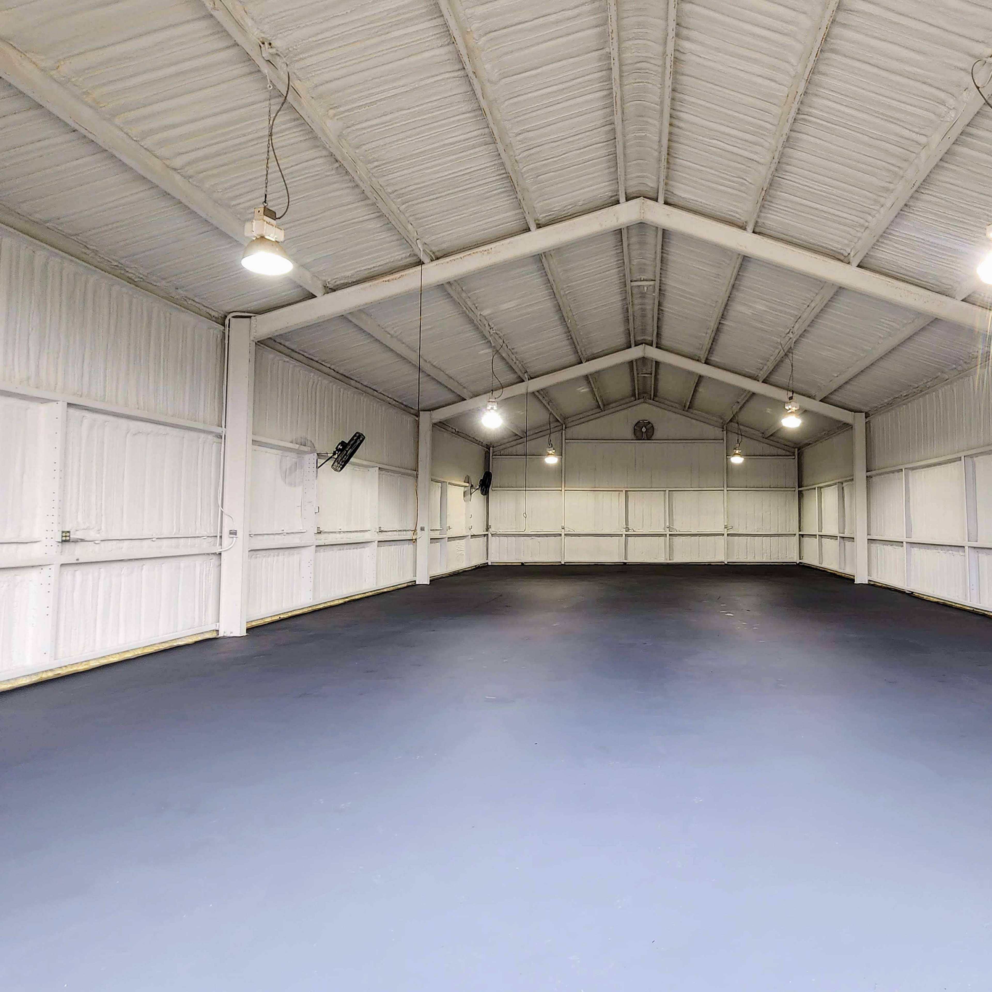 A large, empty warehouse with a high ceiling and concrete floor, illuminated by overhead lights.