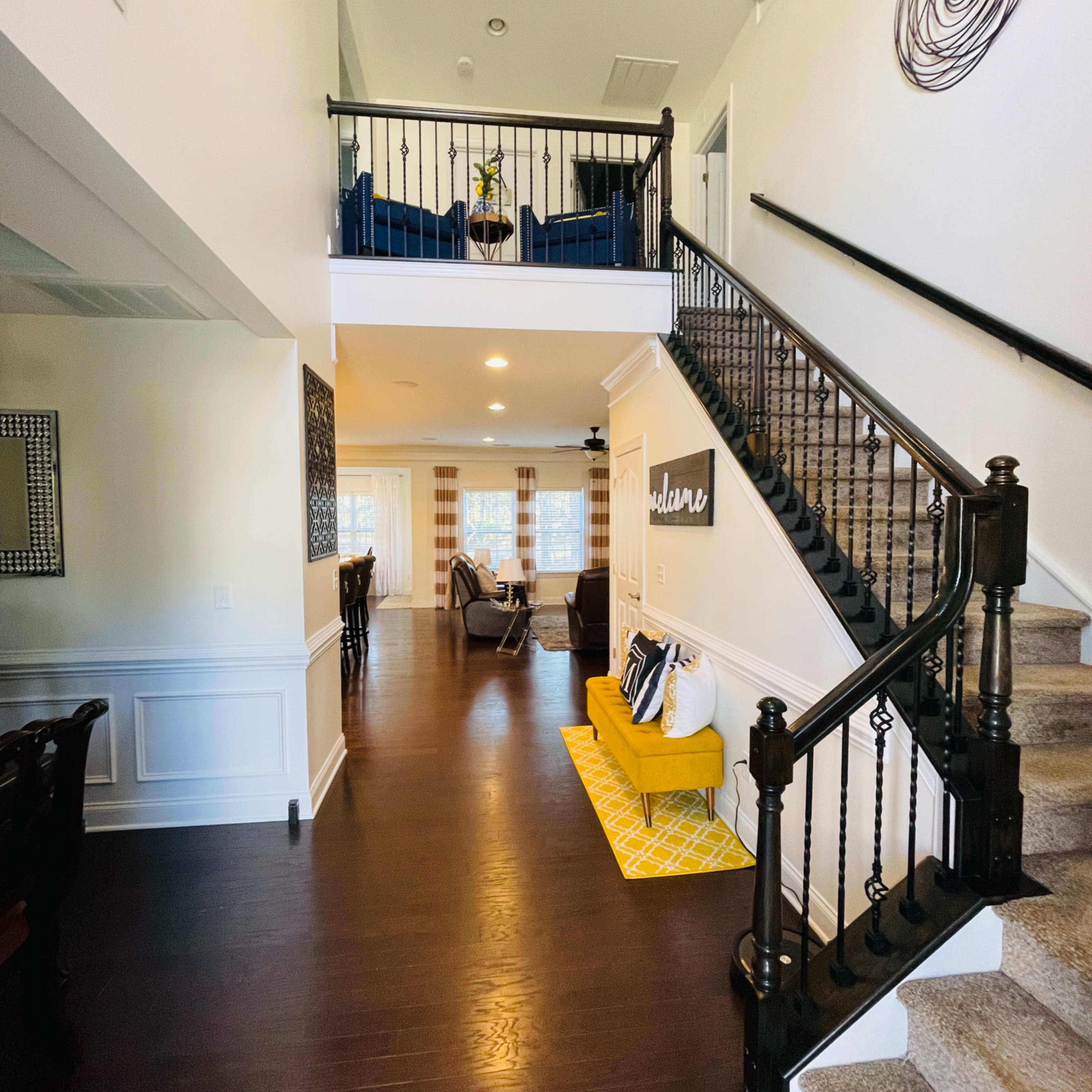 A two-story foyer with a staircase, a yellow bench, and seating areas visible on both levels.