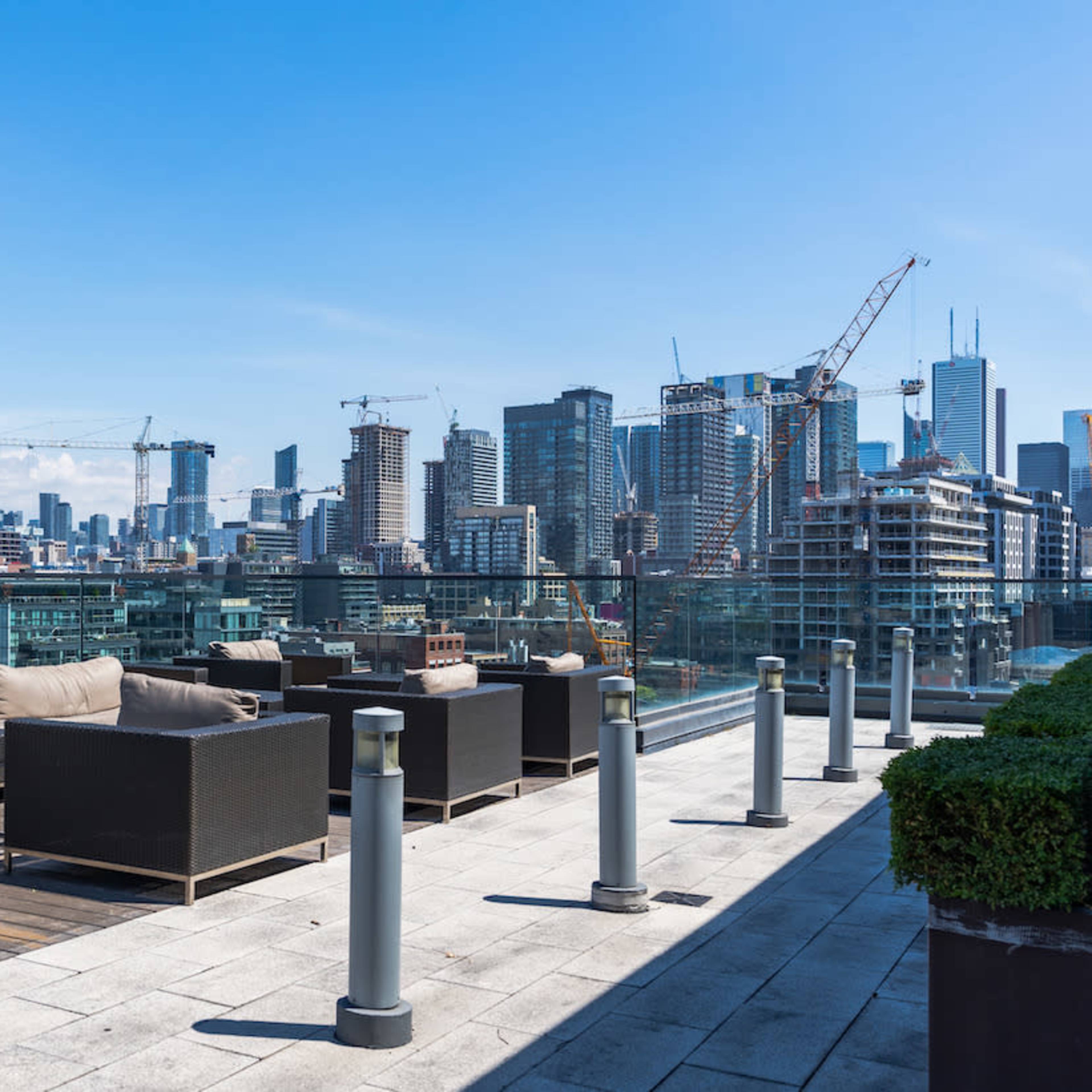 A rooftop terrace features seating and a panoramic view of a city skyline under a clear blue sky.
