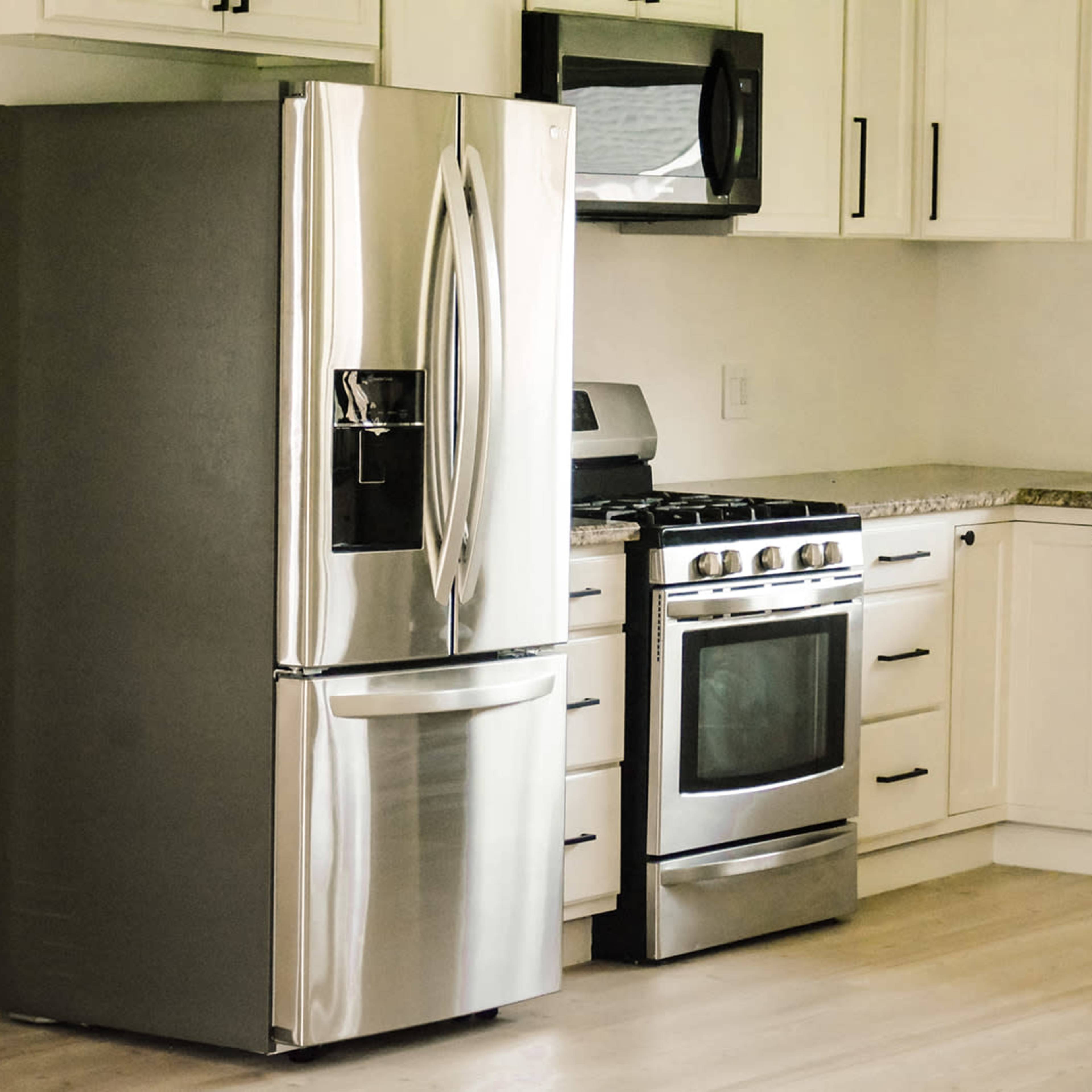 A modern kitchen featuring a stainless steel refrigerator, a gas stove, and white cabinetry with a light wood floor.