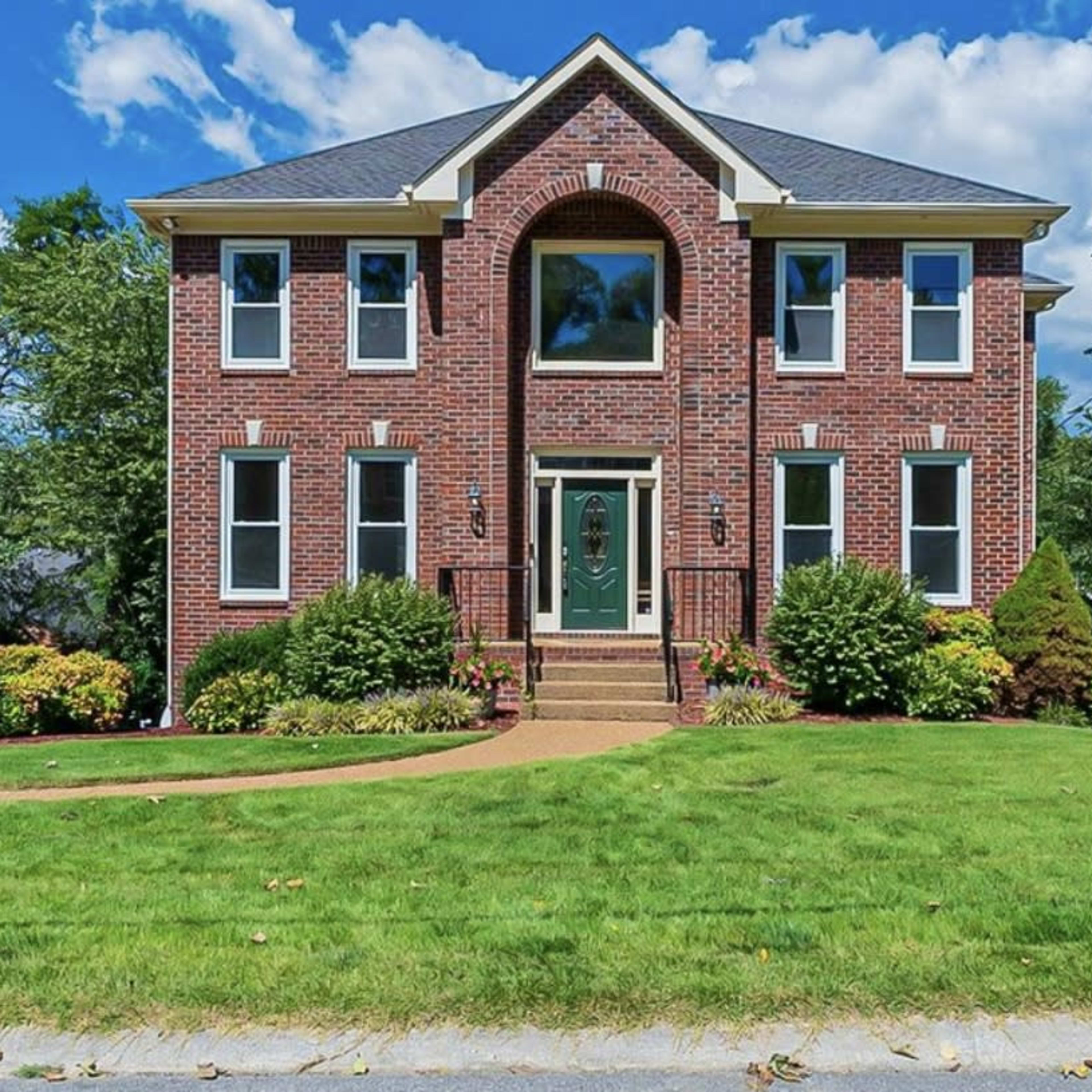 A large brick home with multiple windows and a symmetrical facade sits on a well-maintained lawn.