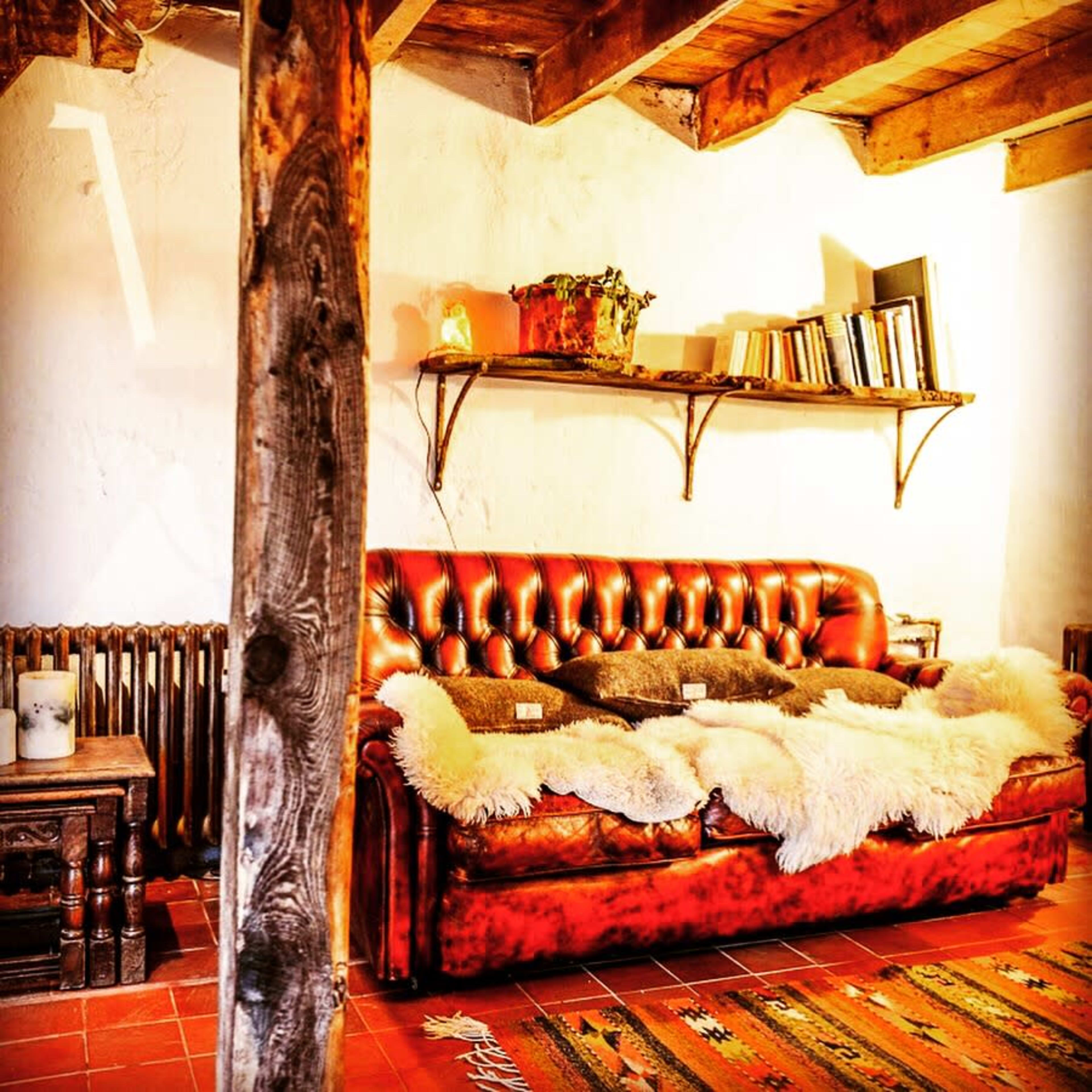 A cozy living room featuring a red leather sofa adorned with a fur throw, wooden shelves filled with books, and a rustic wooden beam supporting the ceiling.