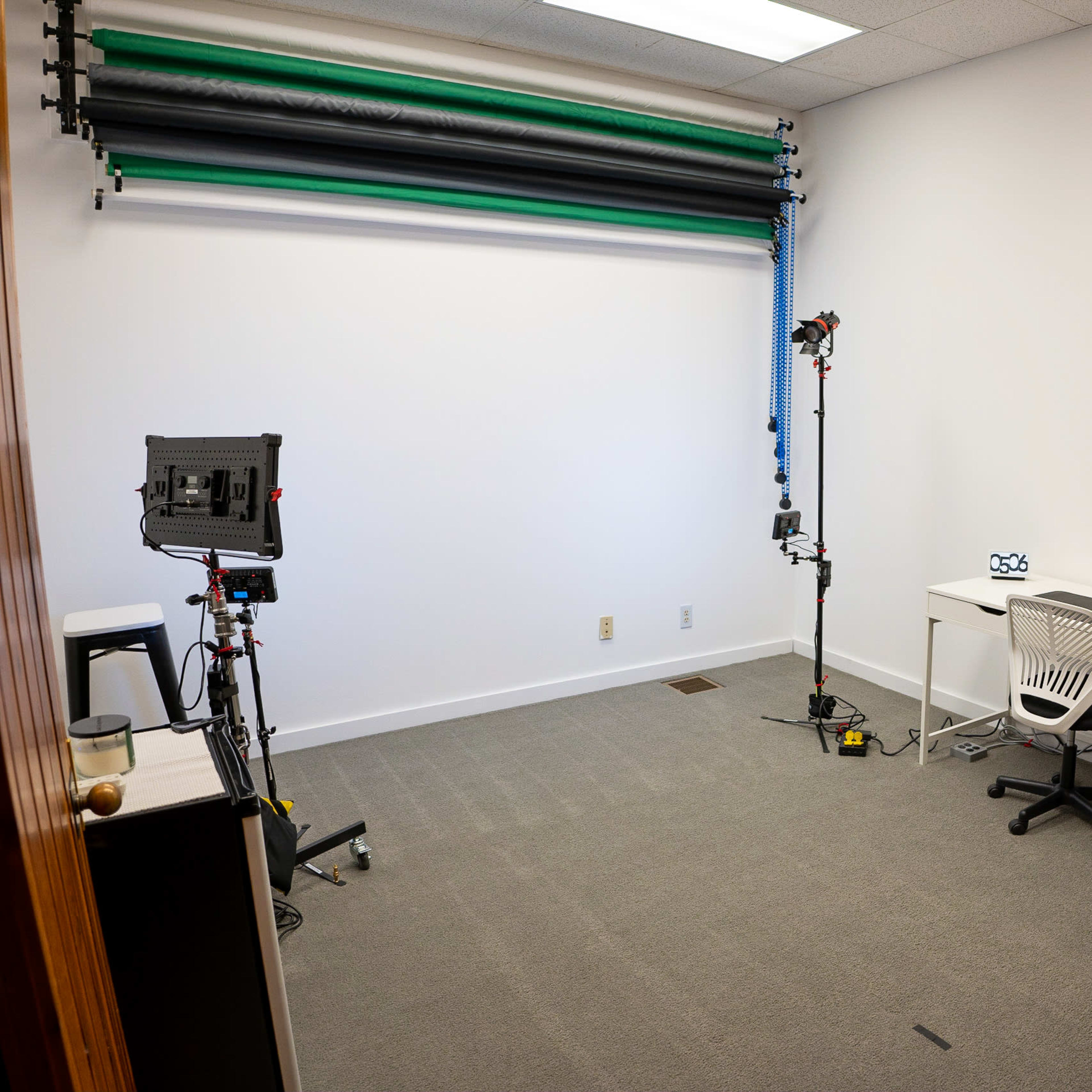 A vacant office space with a white wall, a desk, a chair, and photography equipment in the corners.