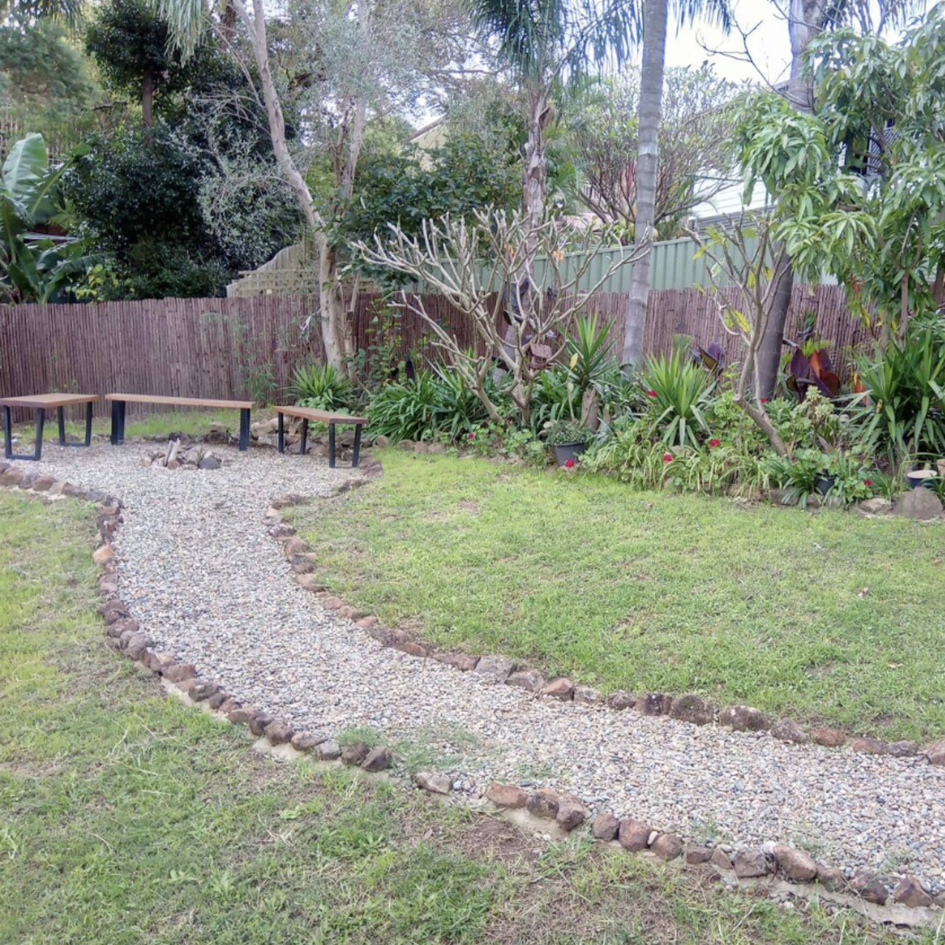 A curved gravel path leads through a landscaped garden with various shrubs and plants, bordered by a low stone wall.