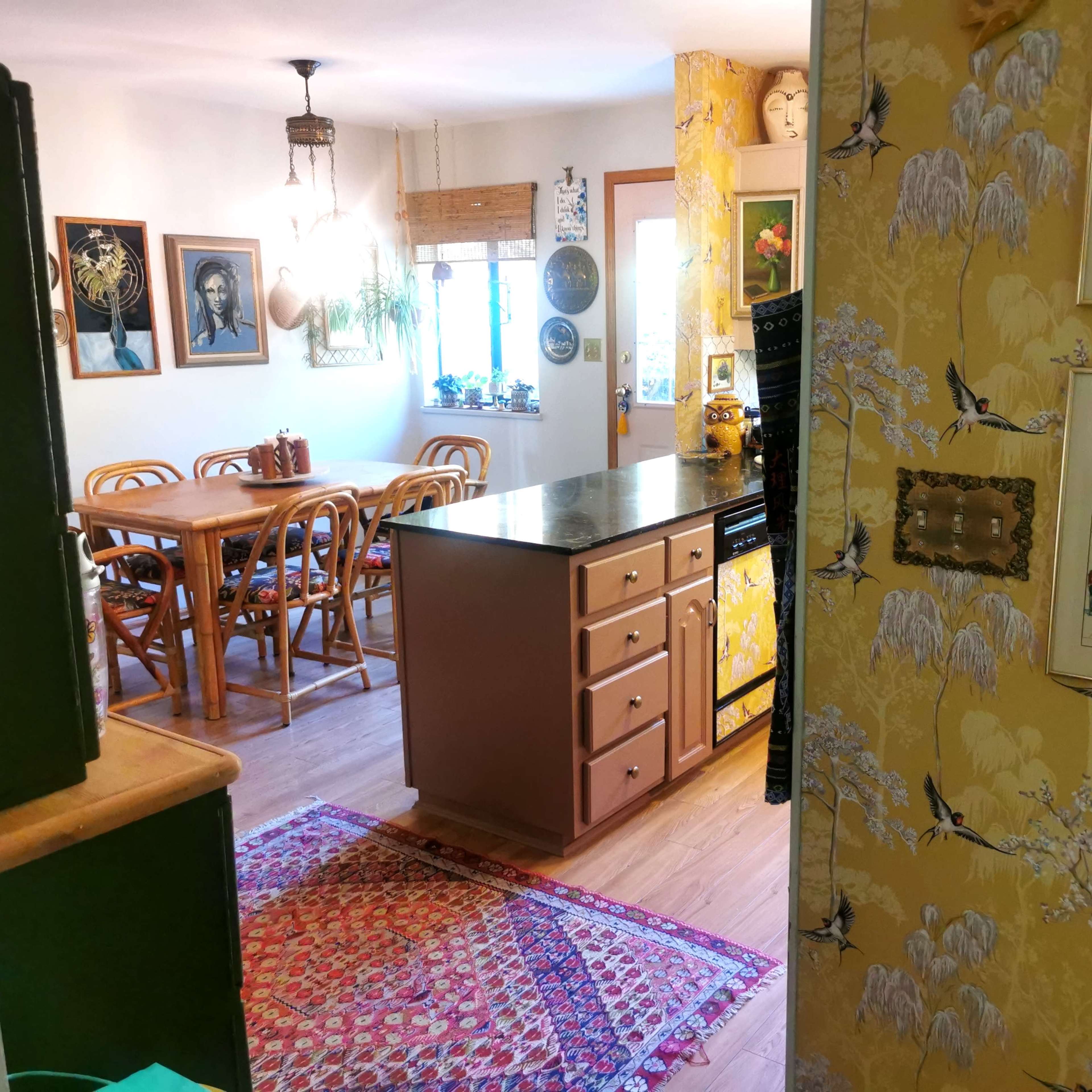 A kitchen and dining area feature wooden furniture, decorative wall art, and patterned wallpaper.