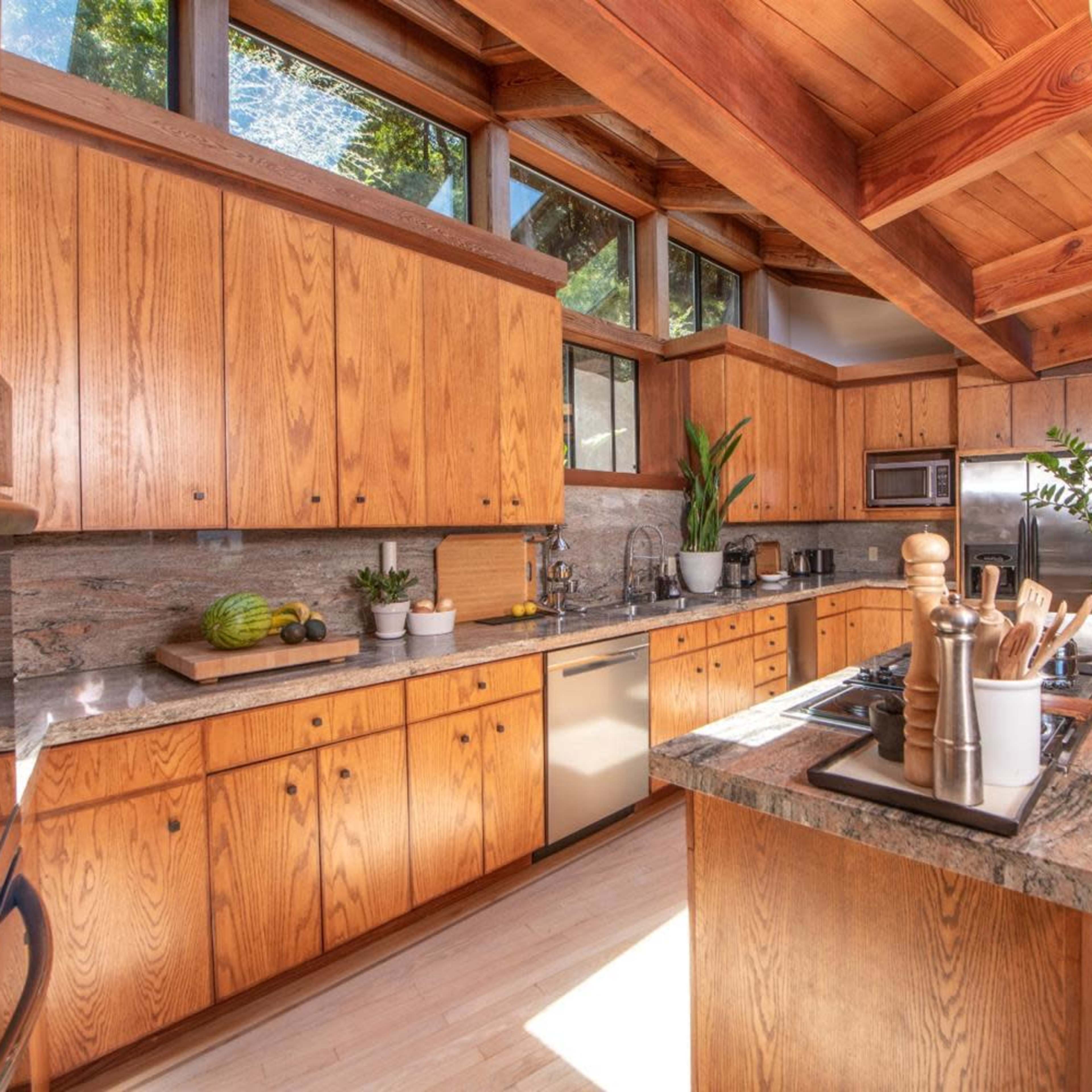 The kitchen features wooden cabinets, a granite countertop, and ample natural light from large windows.