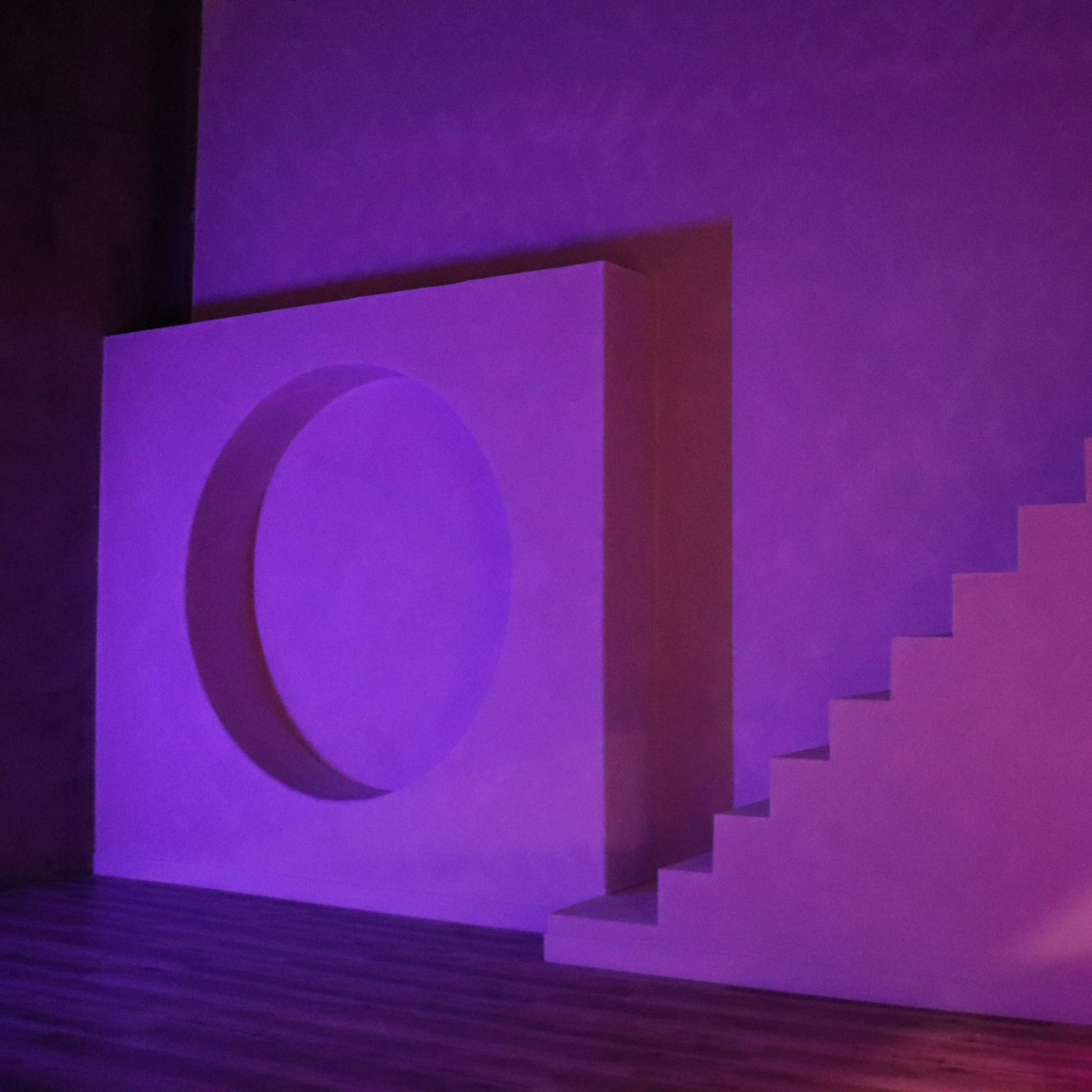 A minimalist interior featuring a curved wall segment, a staircase, and an arched doorway, illuminated with a purple light.