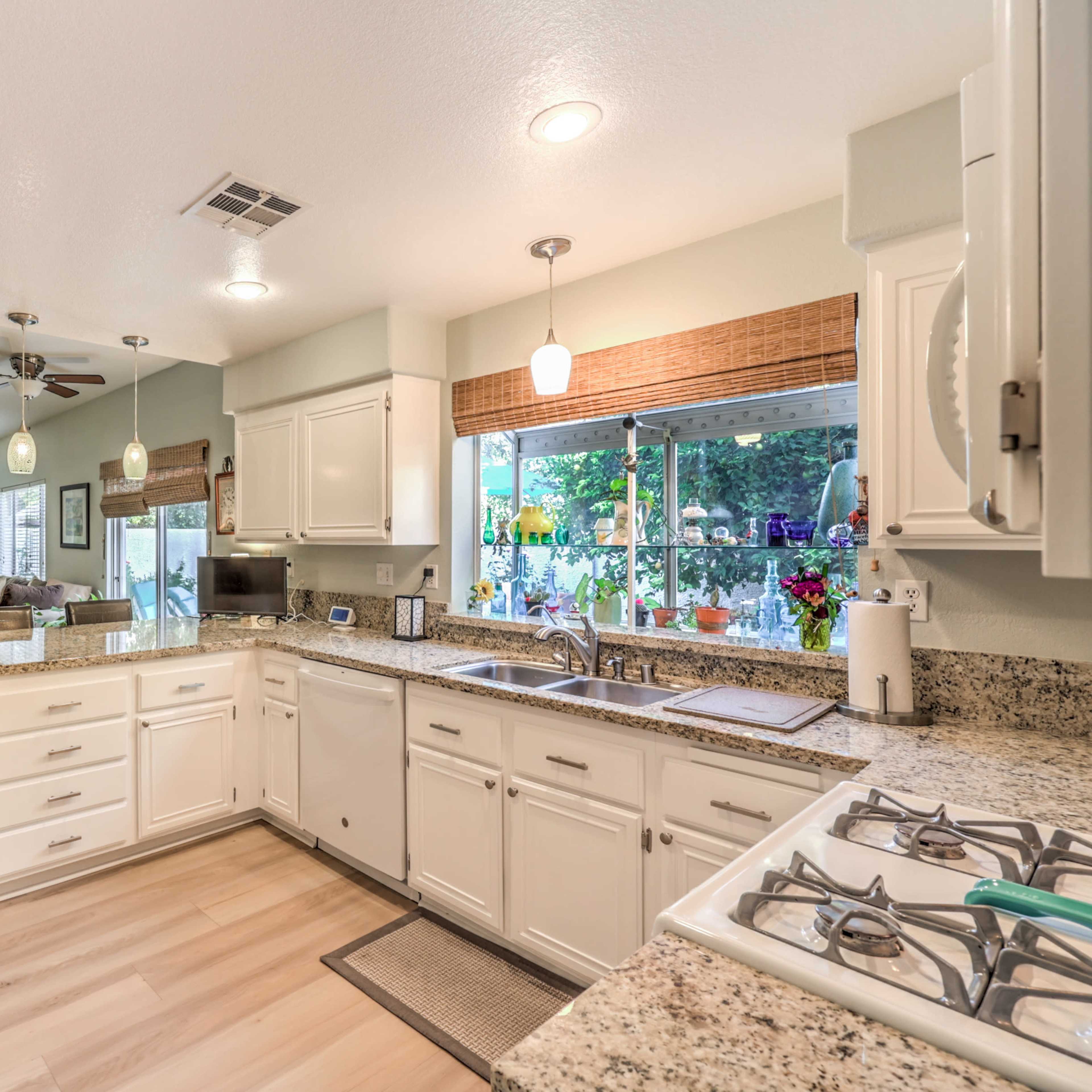 A bright kitchen features white cabinets, granite countertops, and a view into a living area with a fireplace.