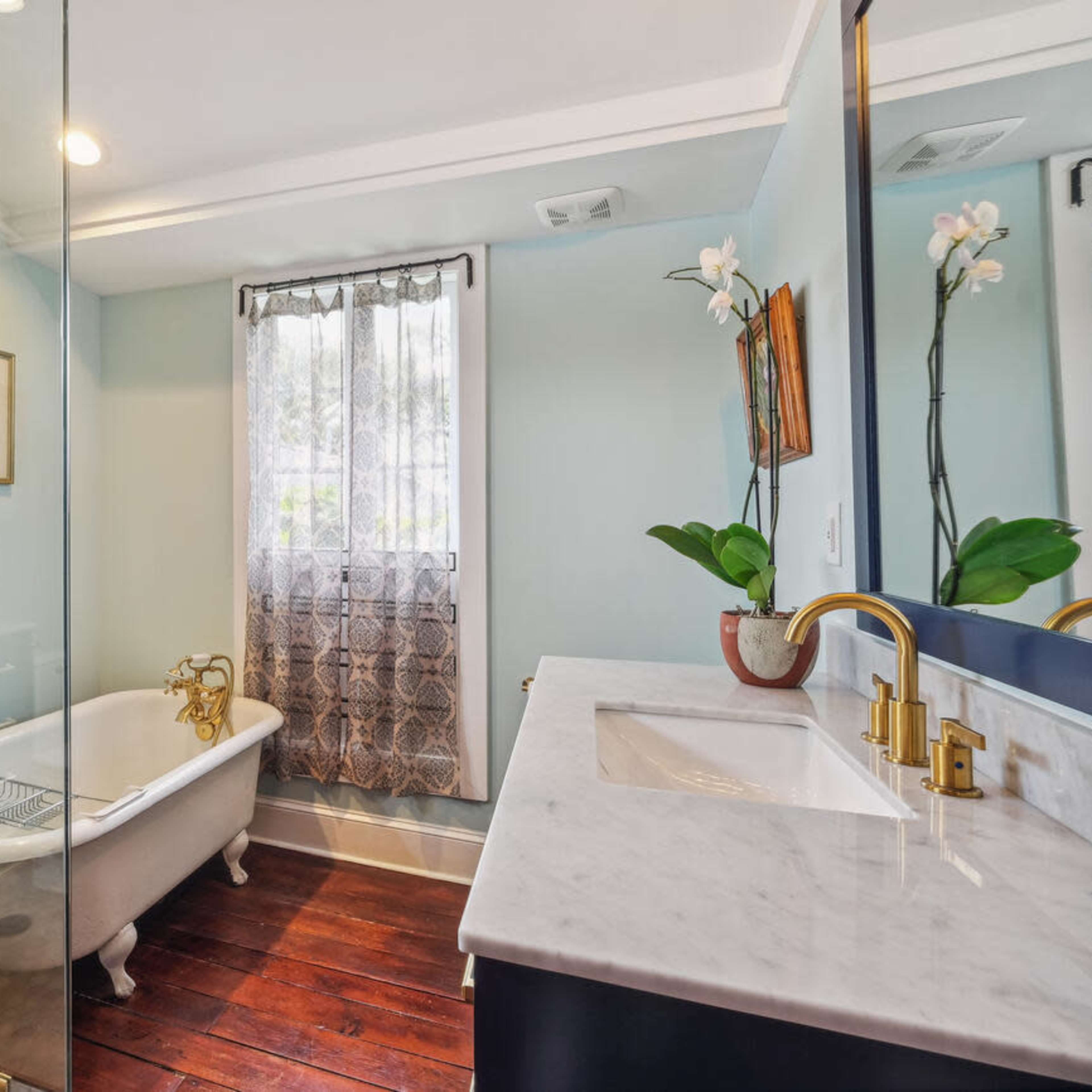 A modern bathroom with a freestanding bathtub, a glass shower enclosure, a marble countertop, and hardwood flooring.
