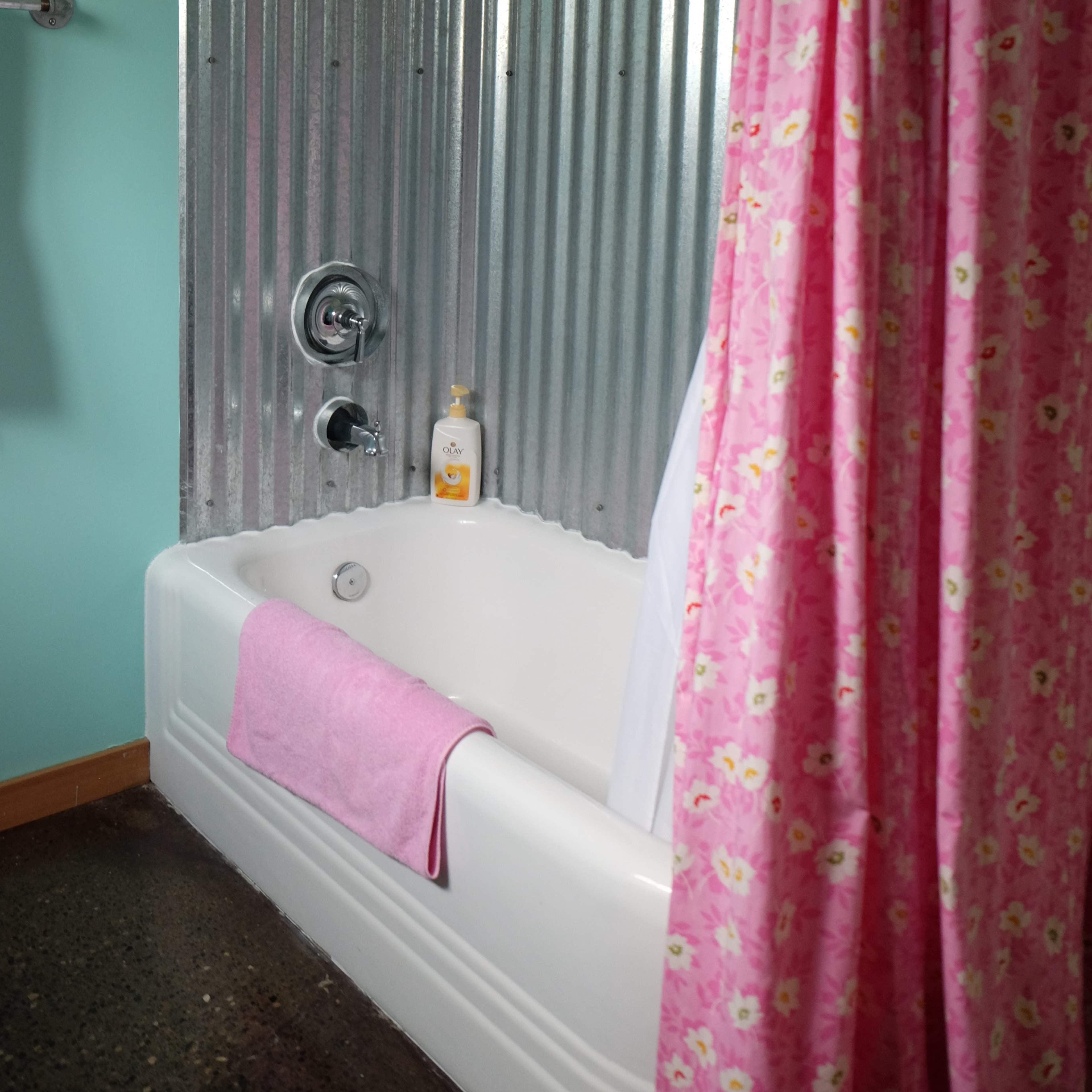A bath area with a white tub, a pink shower curtain, and a corrugated metal shower wall.