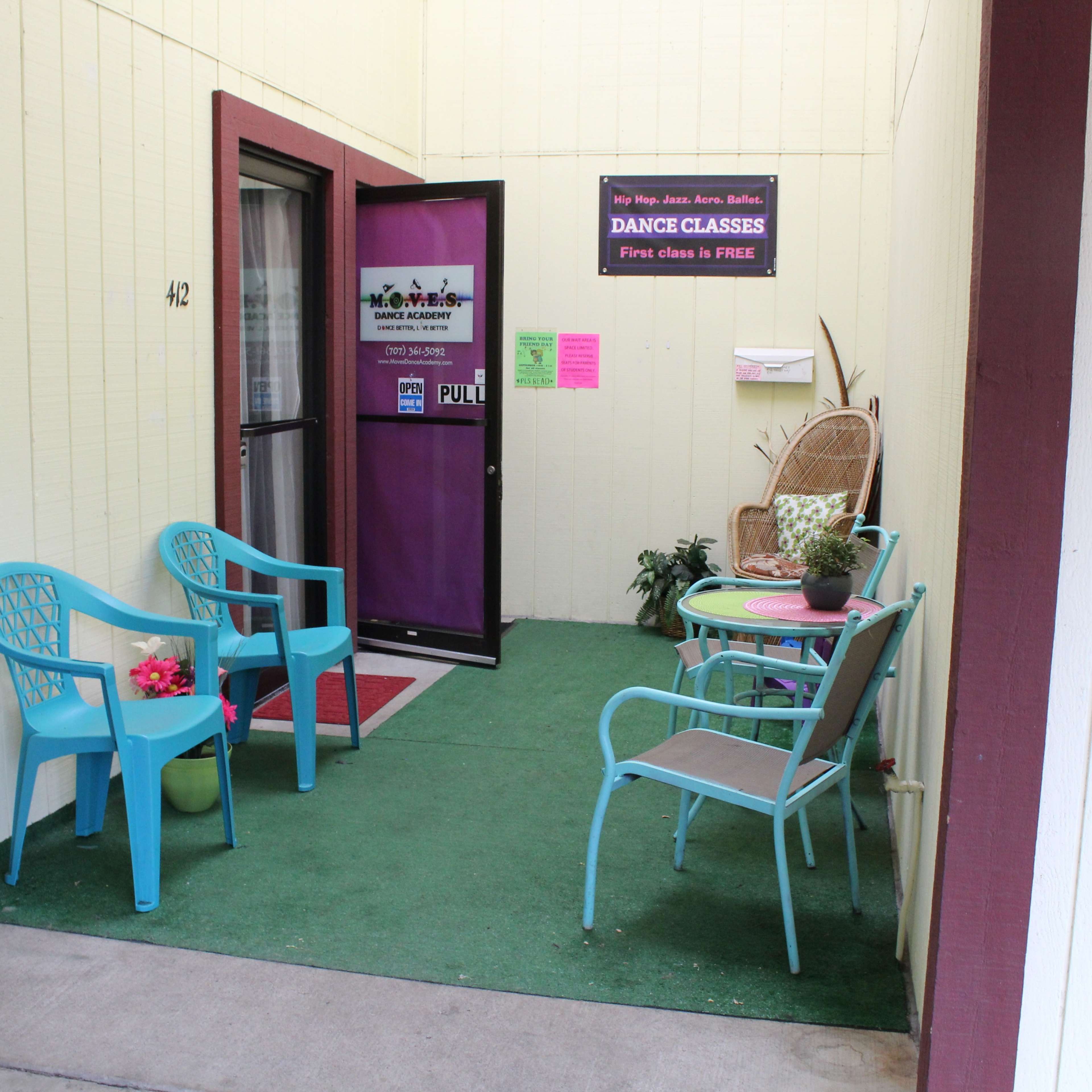 A small entrance area with chairs and a table adorned with plants and a sign for dance classes.