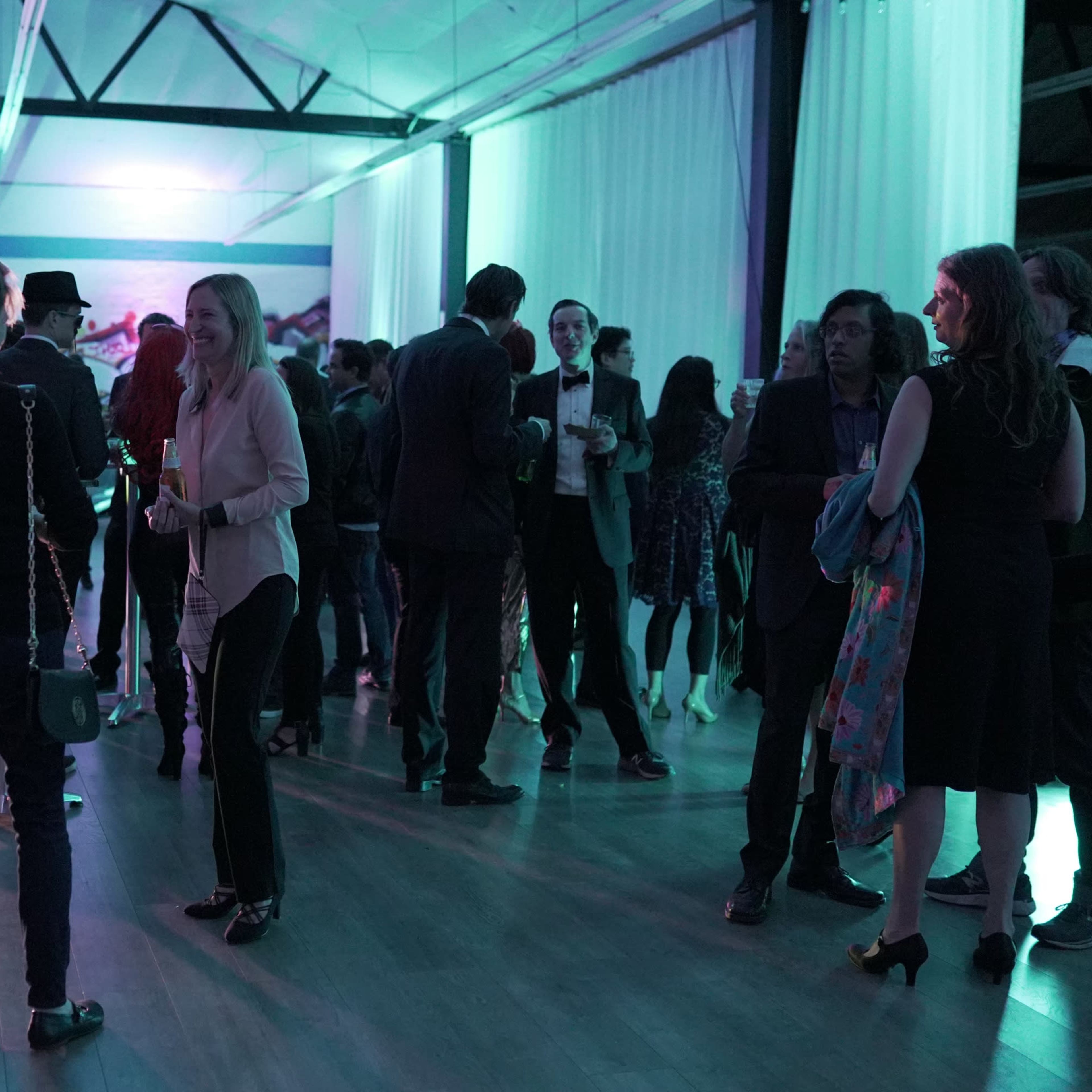 A group of people socialize at a modern event space with colorful lighting and a mural in the background.