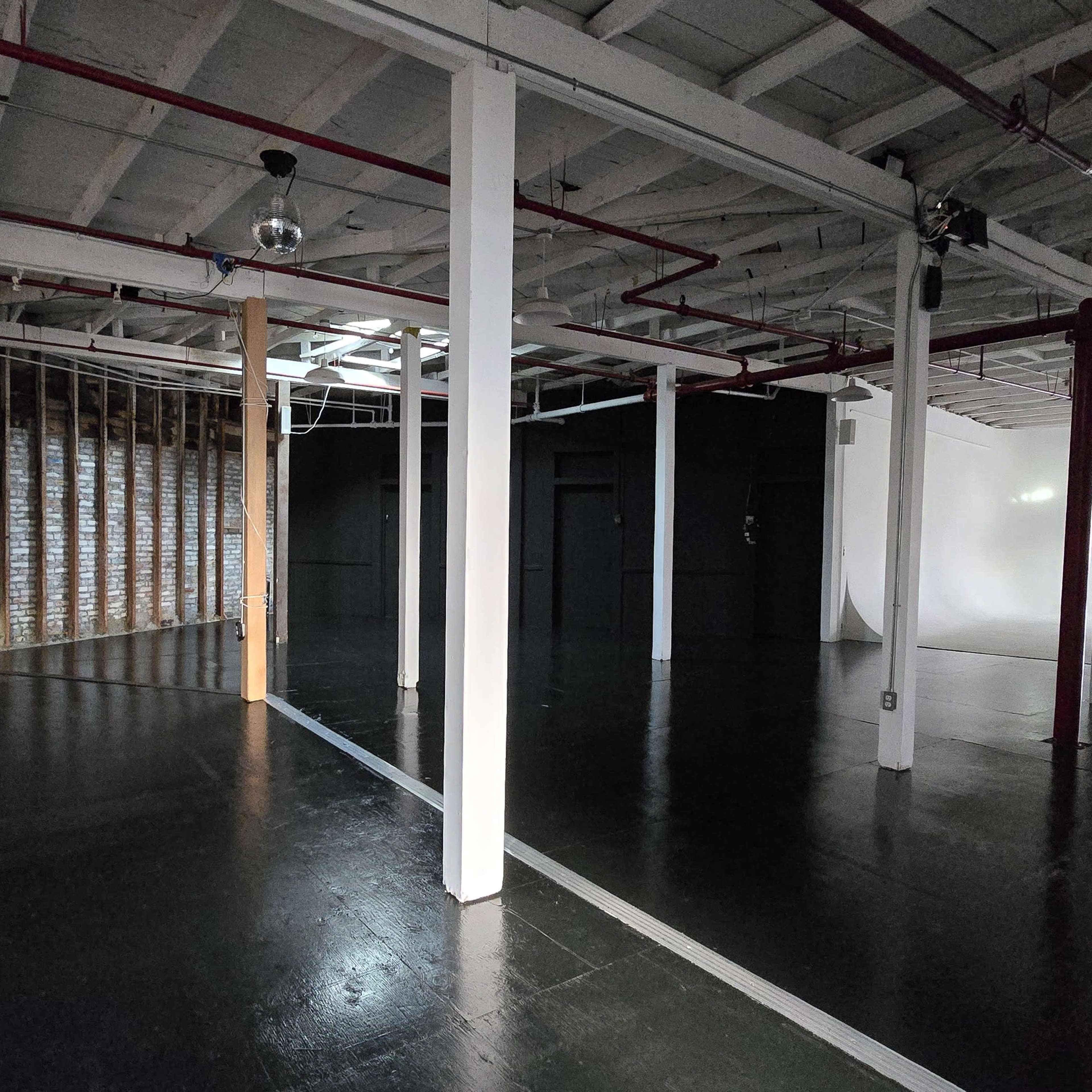 An empty industrial-style space with exposed brick walls, wooden beams, and distinct sections divided by pillars.