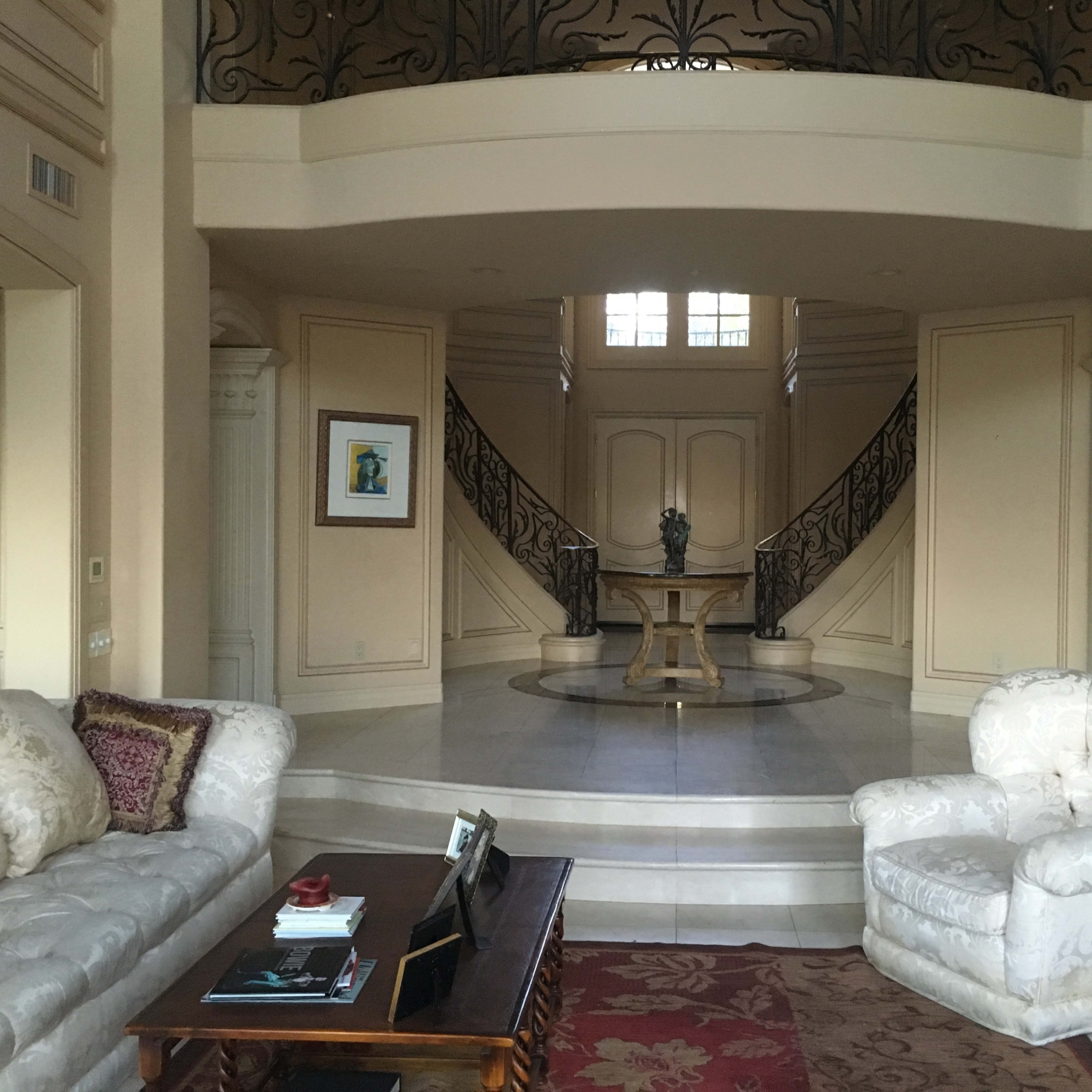 A spacious entryway featuring a marble floor, a round table, and a staircase with decorative railings leading to an upper level.