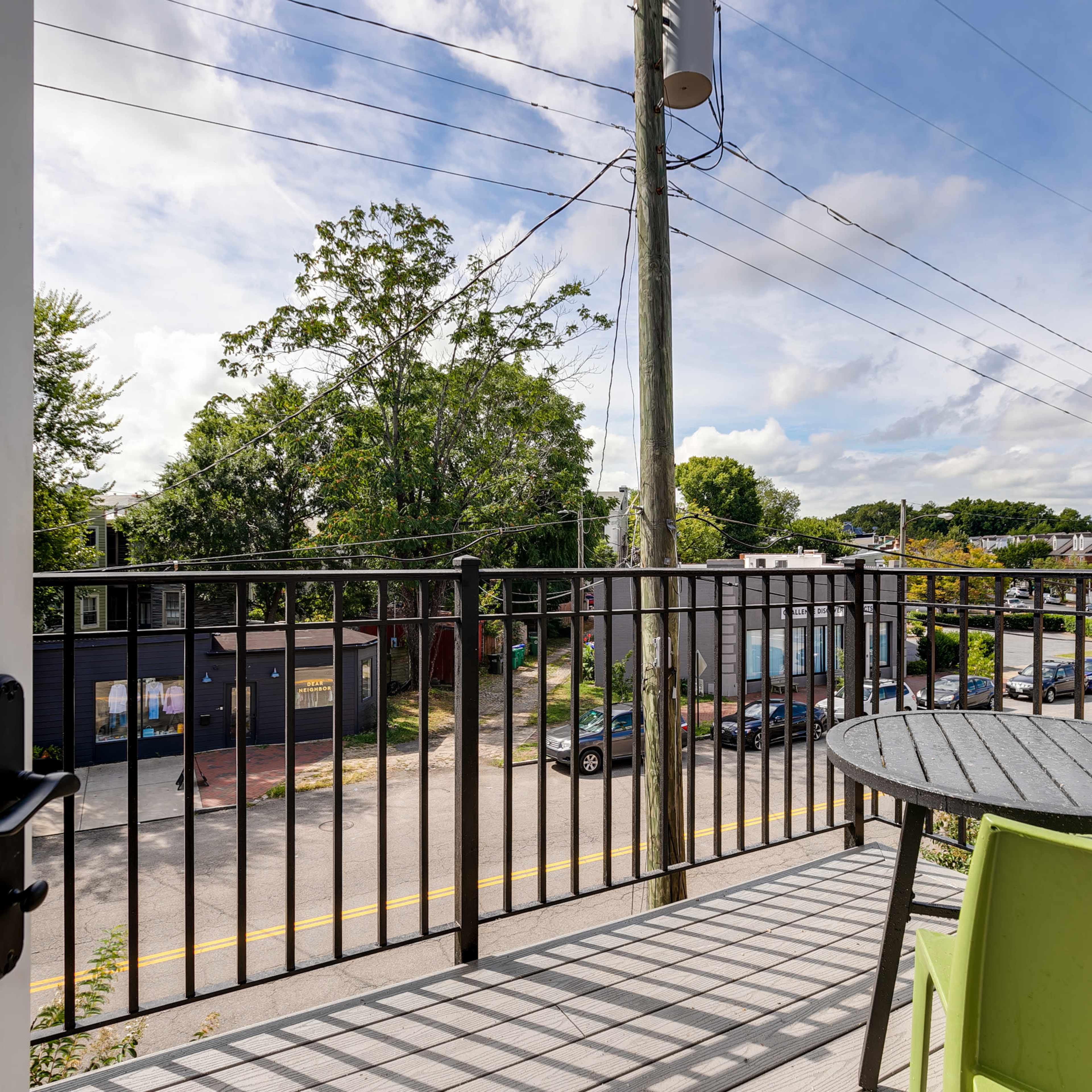 A balcony view shows a street lined with parked cars, trees, and utility poles under a cloudy sky.