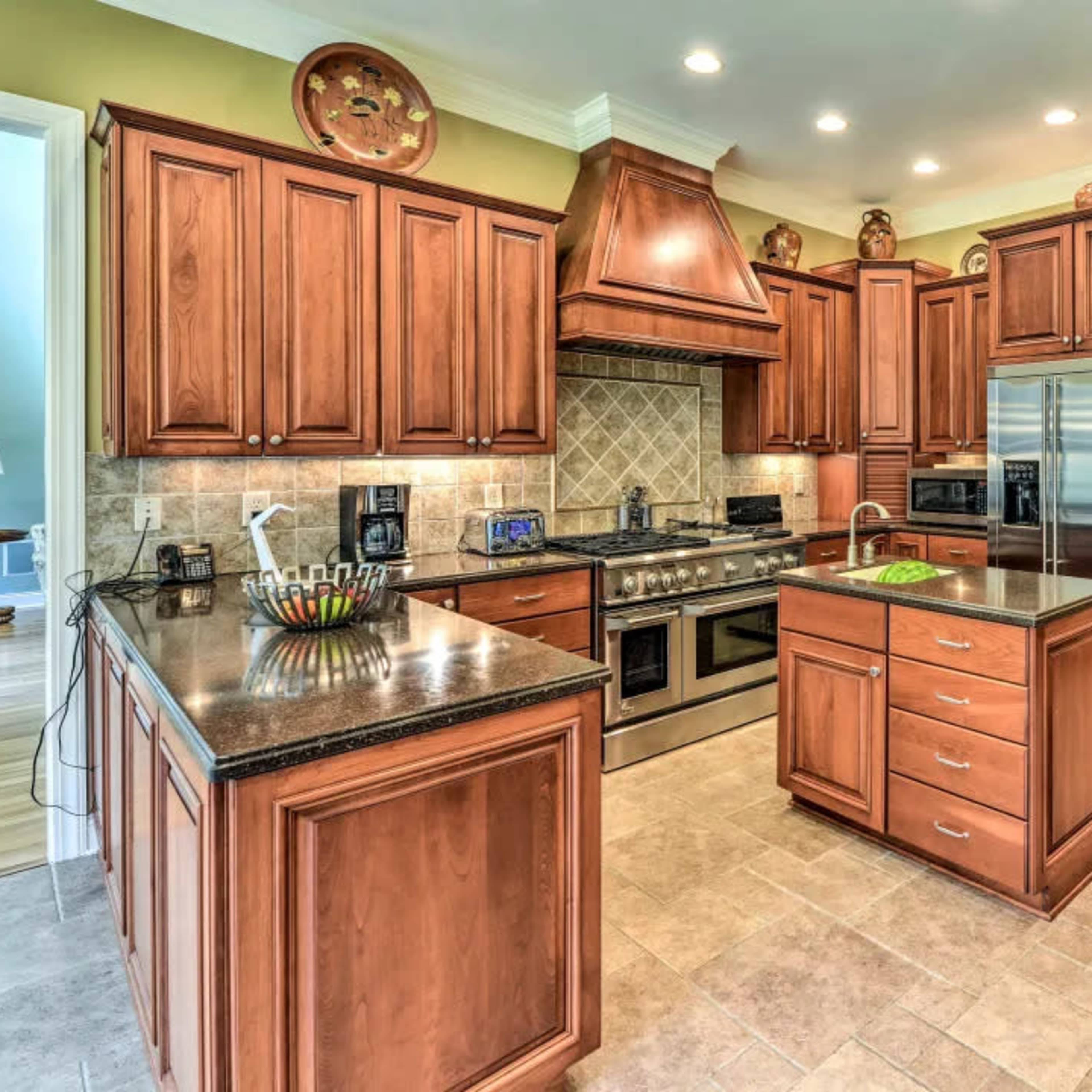 A spacious kitchen featuring wooden cabinets, stainless steel appliances, and a central island with a dark countertop.