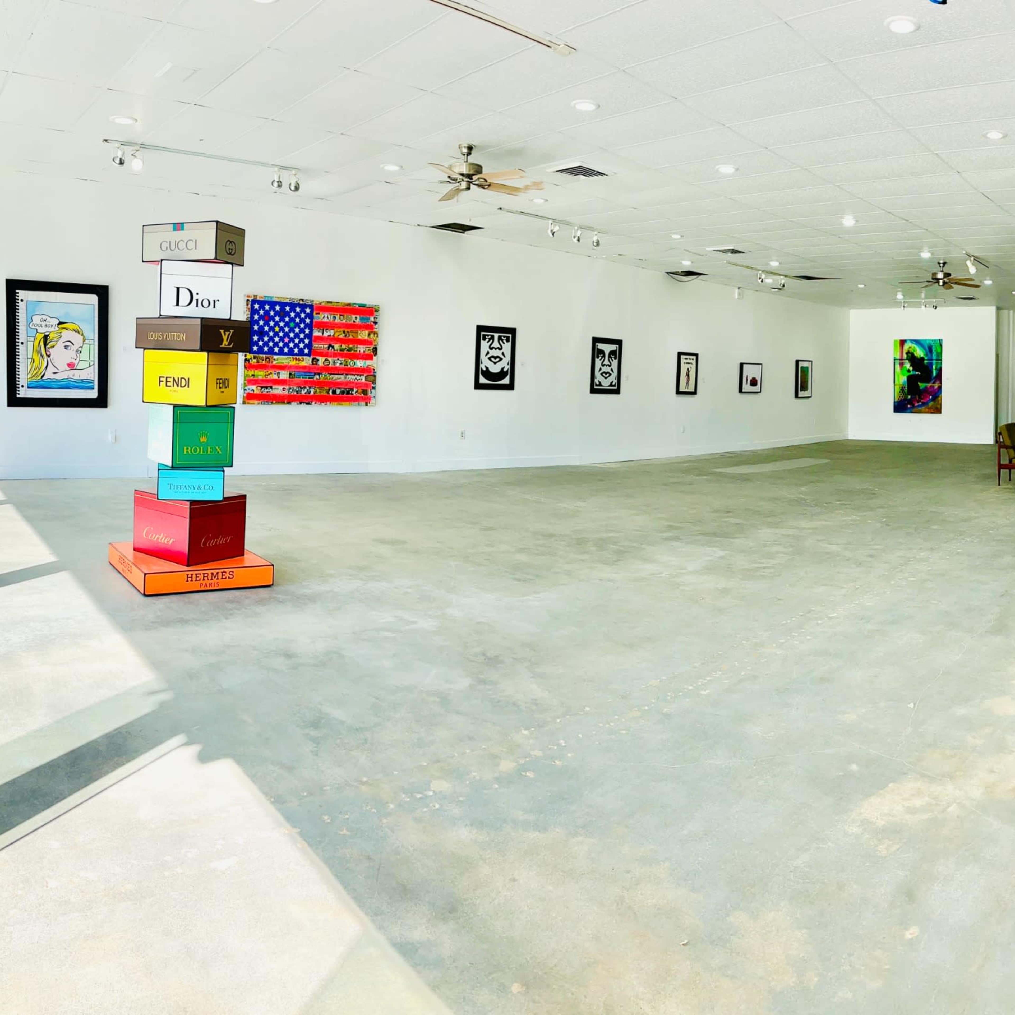 A spacious art gallery featuring rows of framed artworks on white walls and a simple arrangement of furniture in the center.