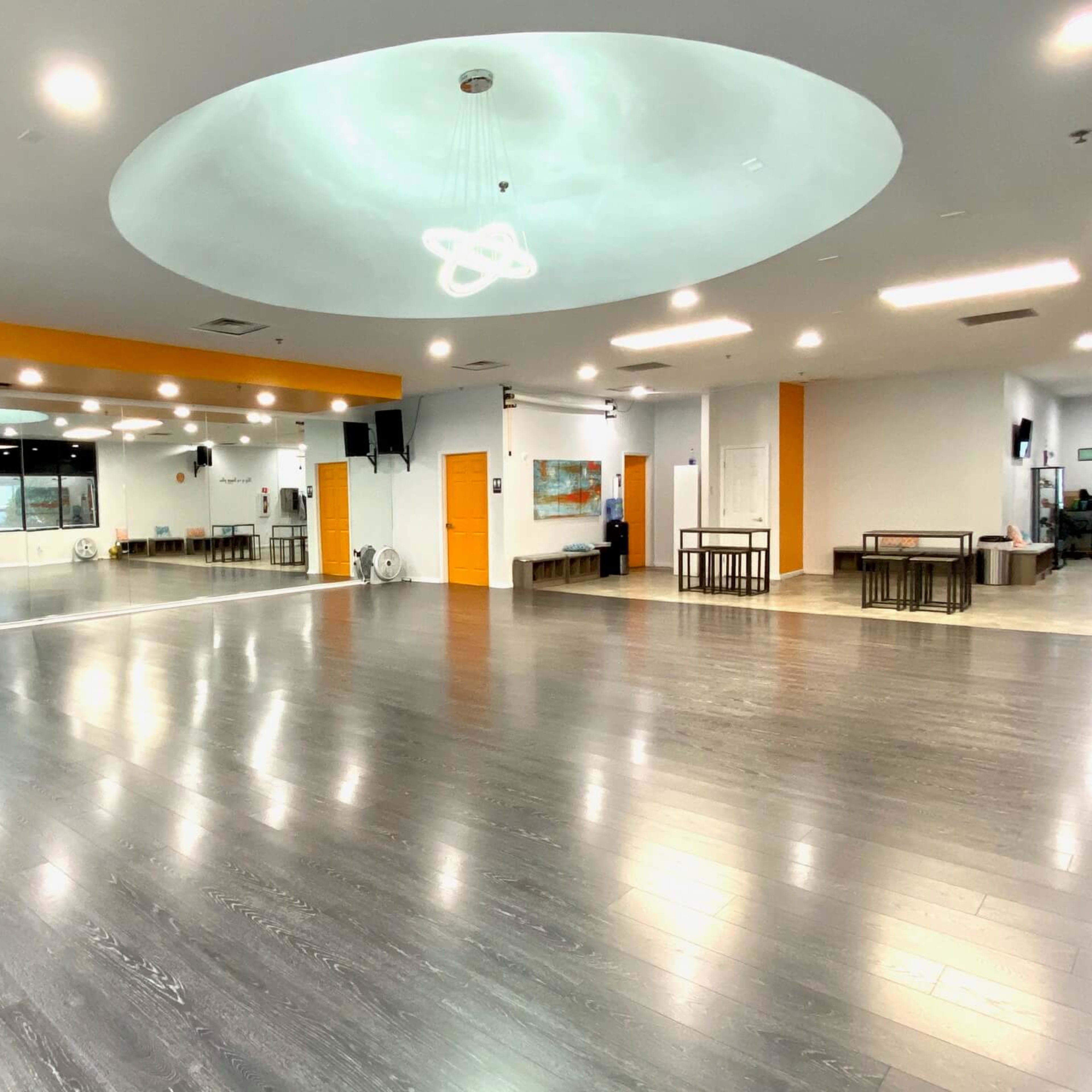 A spacious, well-lit dance studio with a wooden floor, large mirrors, and minimal furniture.
