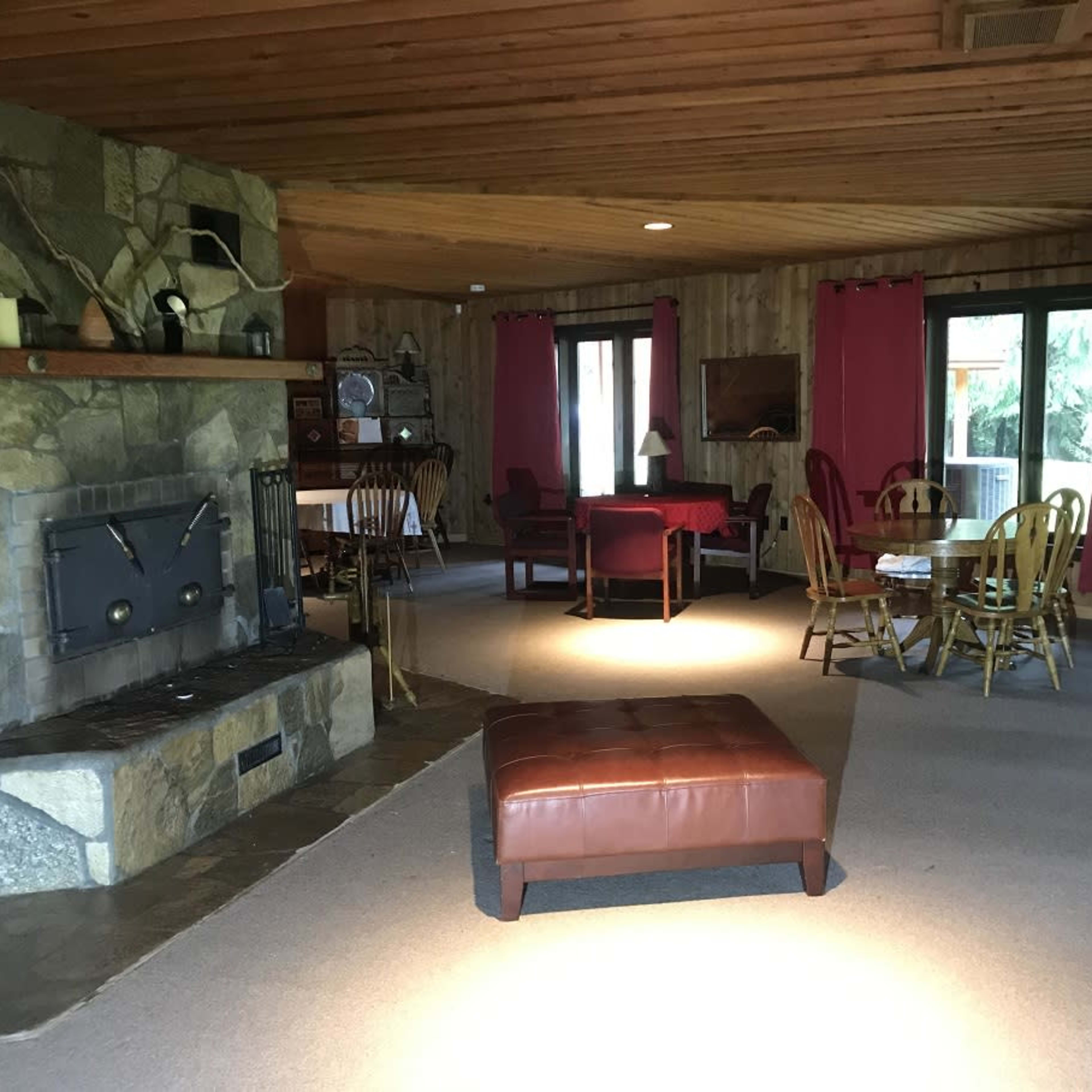 A spacious living area features a stone fireplace, a central ottoman, and a dining table surrounded by wooden chairs.