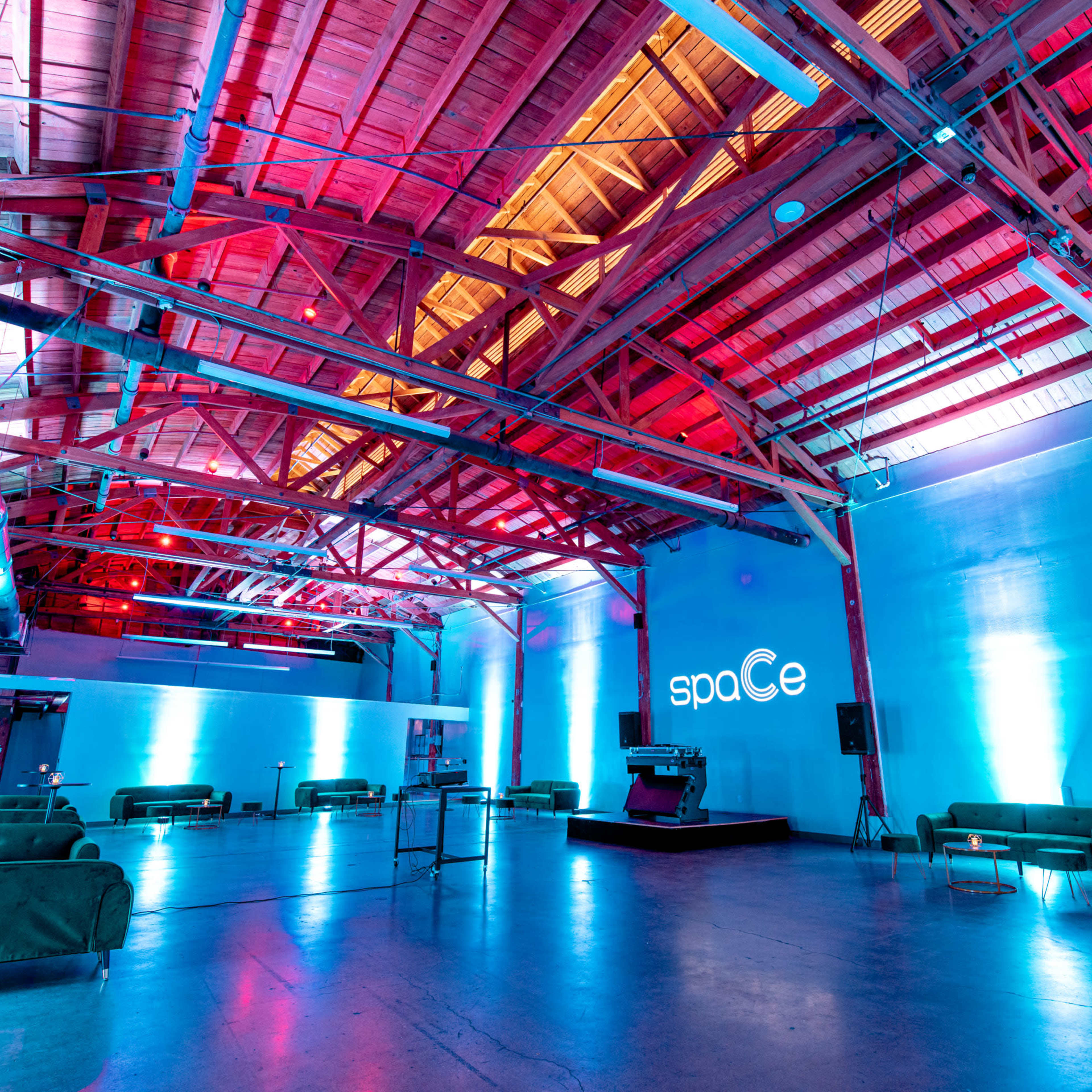 A large, modern event space with colorful lighting, exposed wooden beams, and green couches arranged around the area.