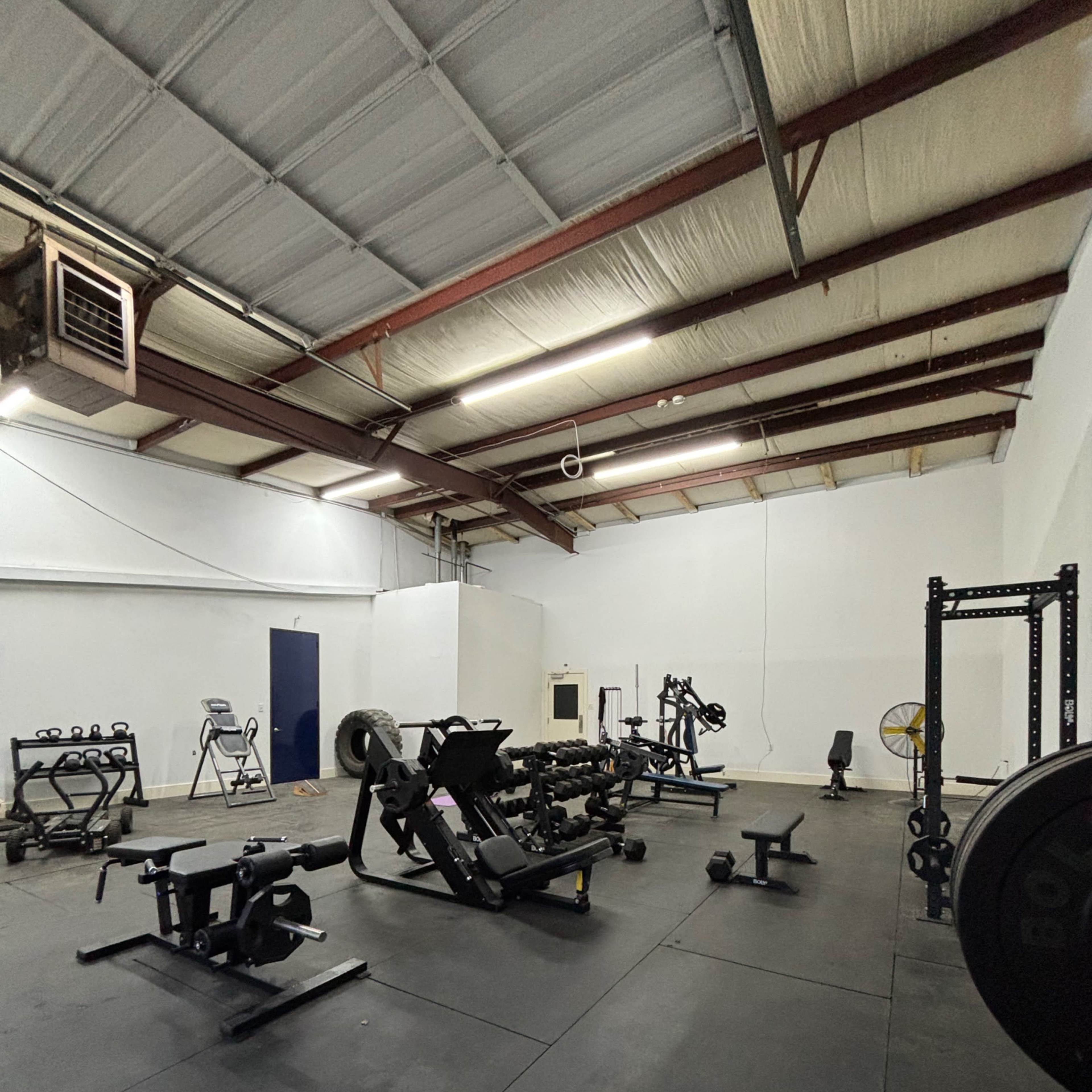 A spacious gym filled with various weightlifting equipment and exercise machines on a rubber flooring surface.