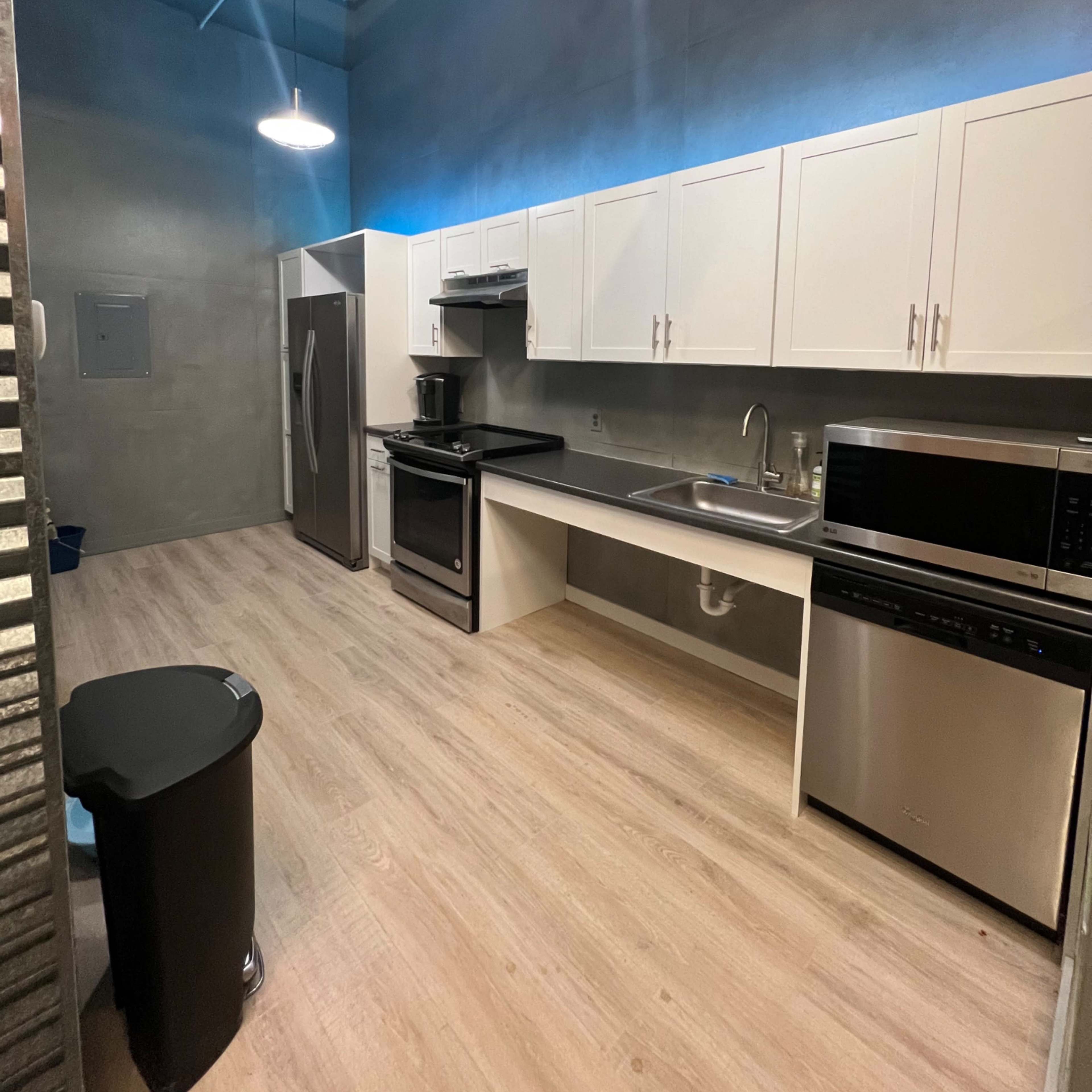 A modern kitchen with white cabinets, stainless steel appliances, and a light wood floor.