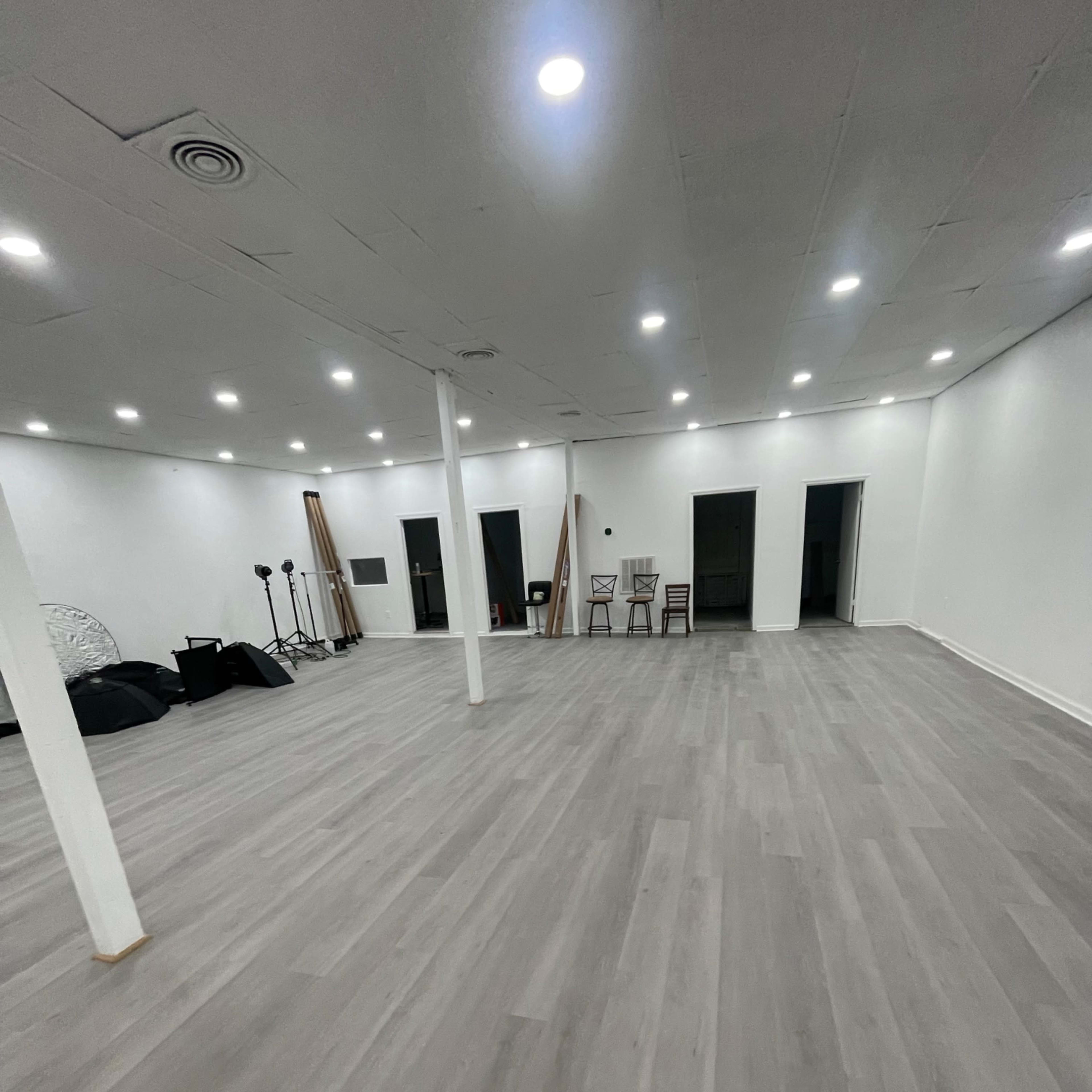 A spacious, empty room with gray wooden flooring, white walls, and several doors along one side.