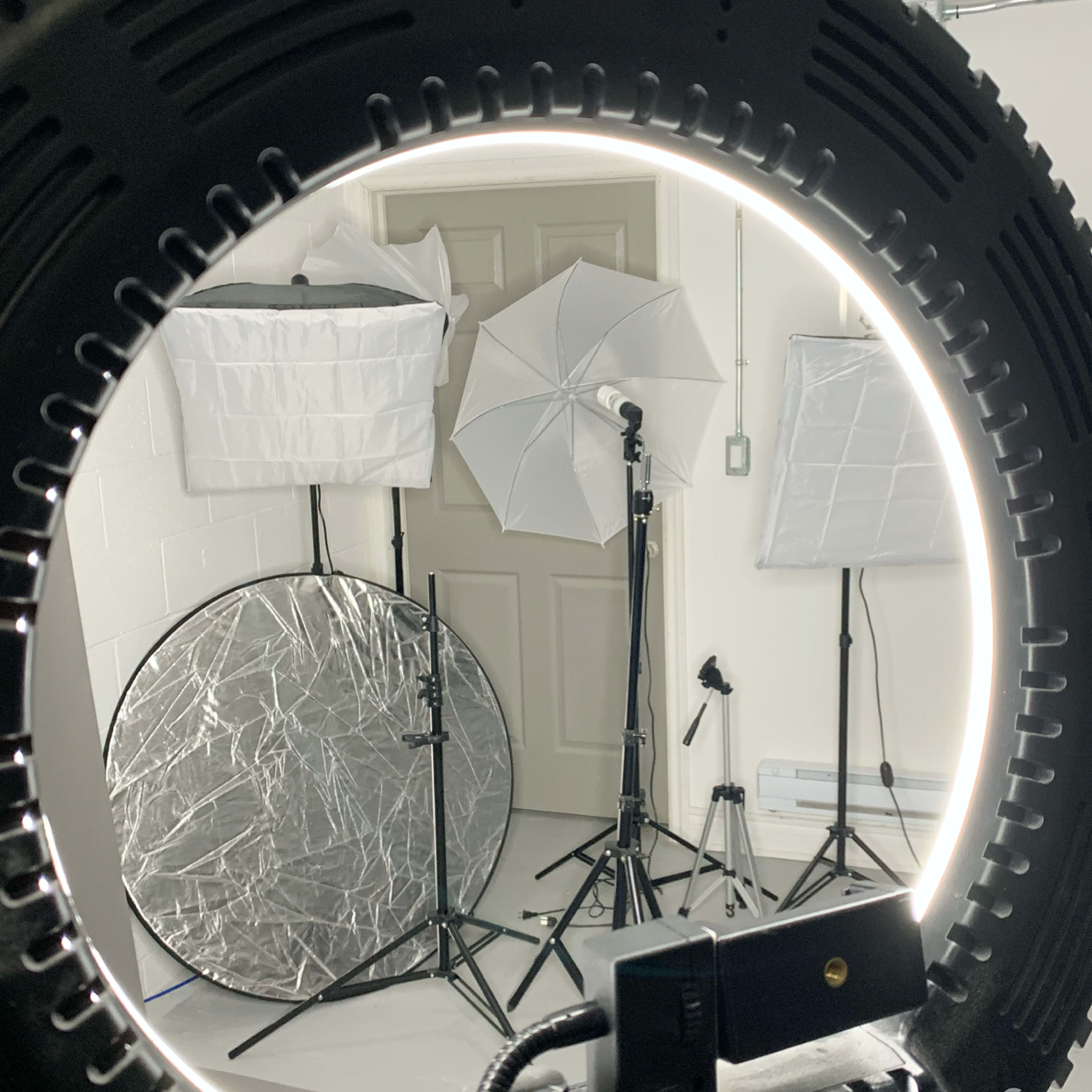A photography studio setup with various light sources, including umbrellas and a circular softbox, arranged in front of a closed door.