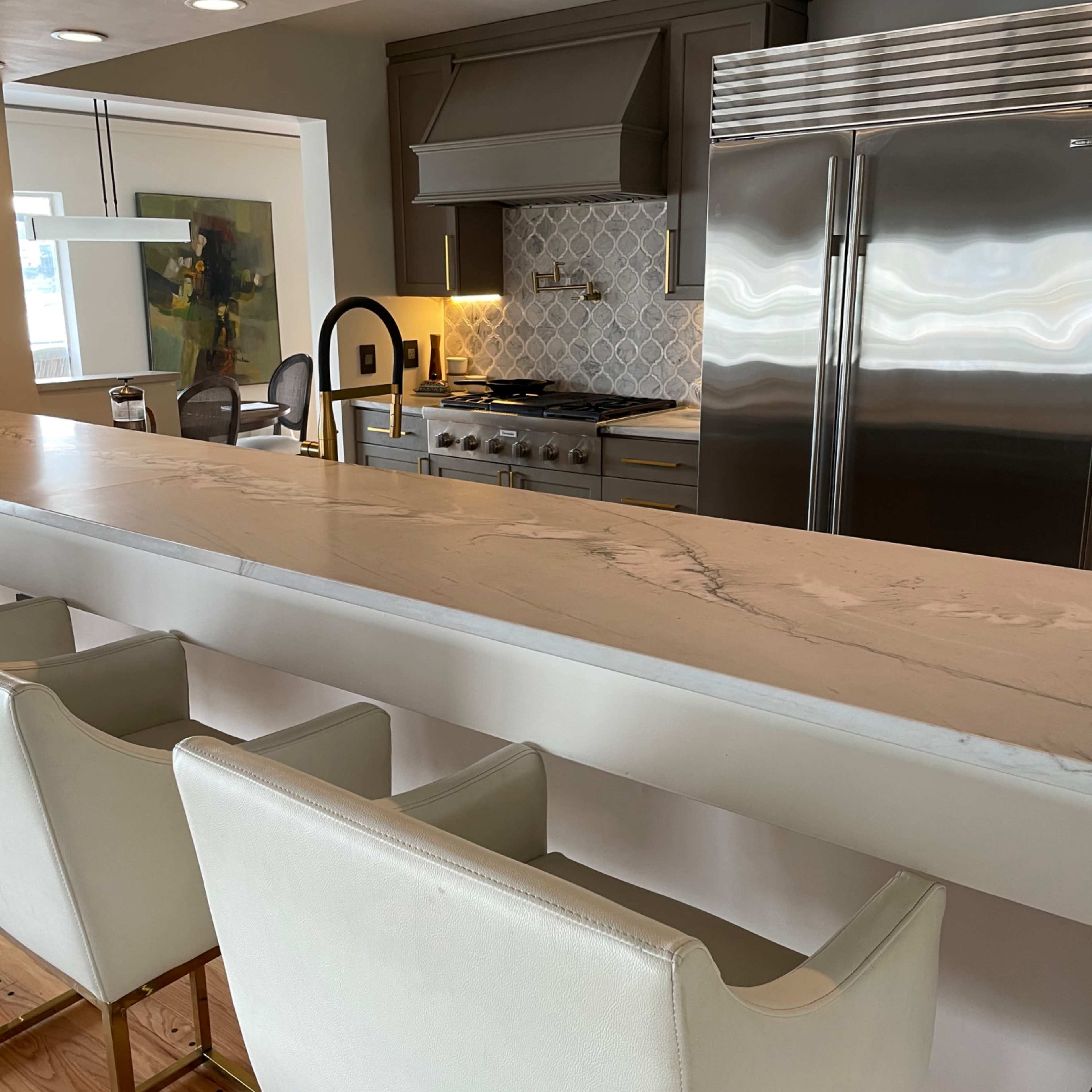 A modern kitchen with a large marble countertop, gray cabinetry, and stainless steel appliances.