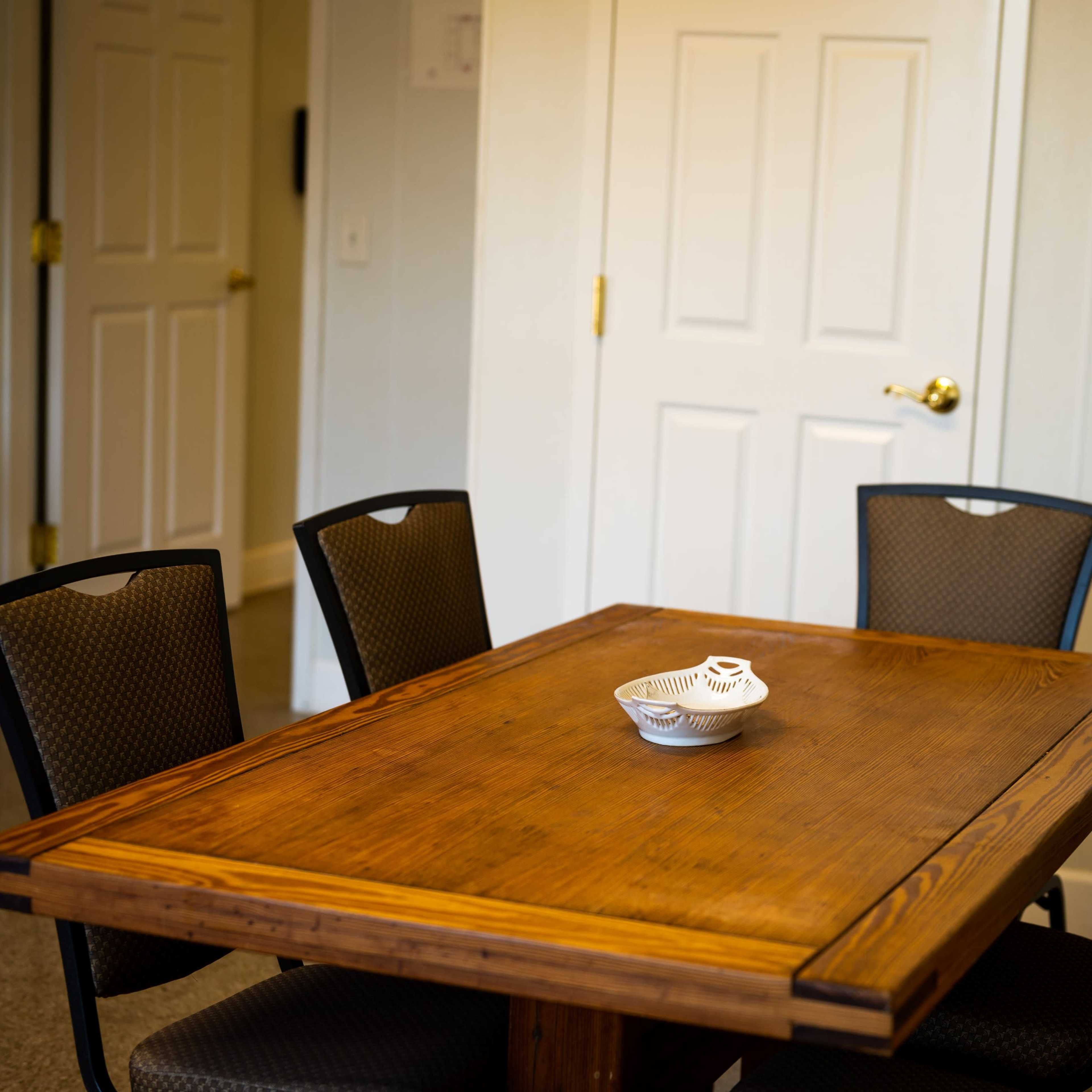 A wooden dining table with a decorative bowl on it is surrounded by four black chairs in a room with two closed doors.