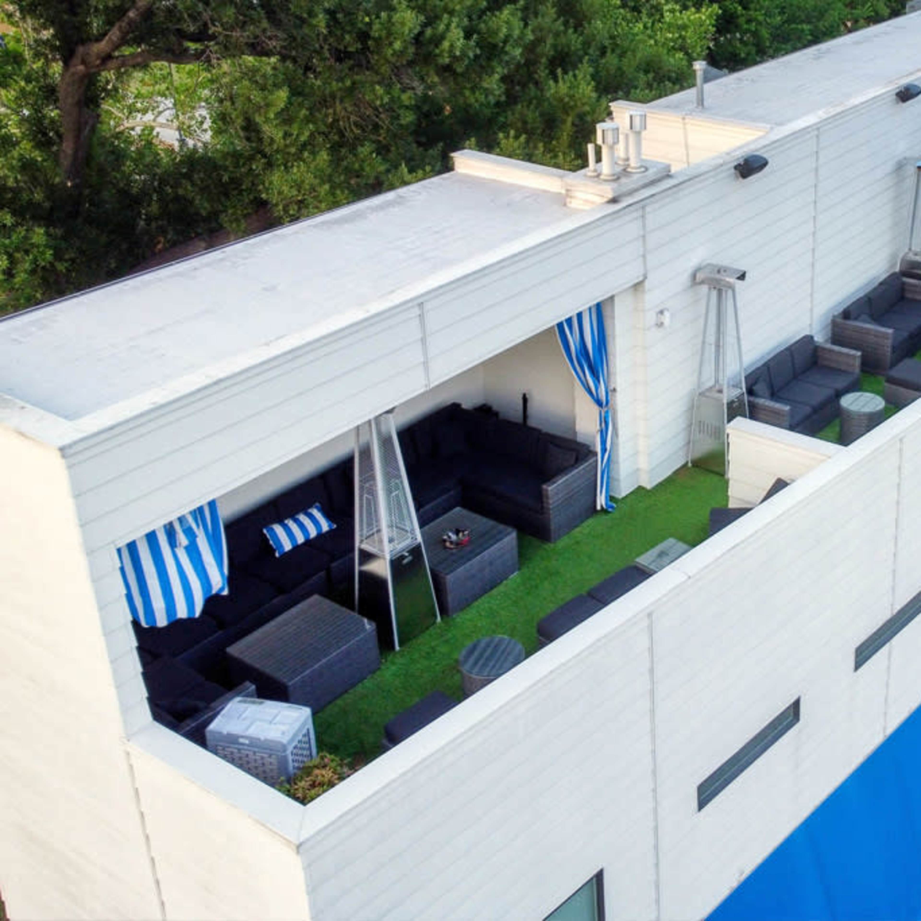 A rooftop terrace featuring several patio furniture sets, green grass-like carpeting, and blue awnings.