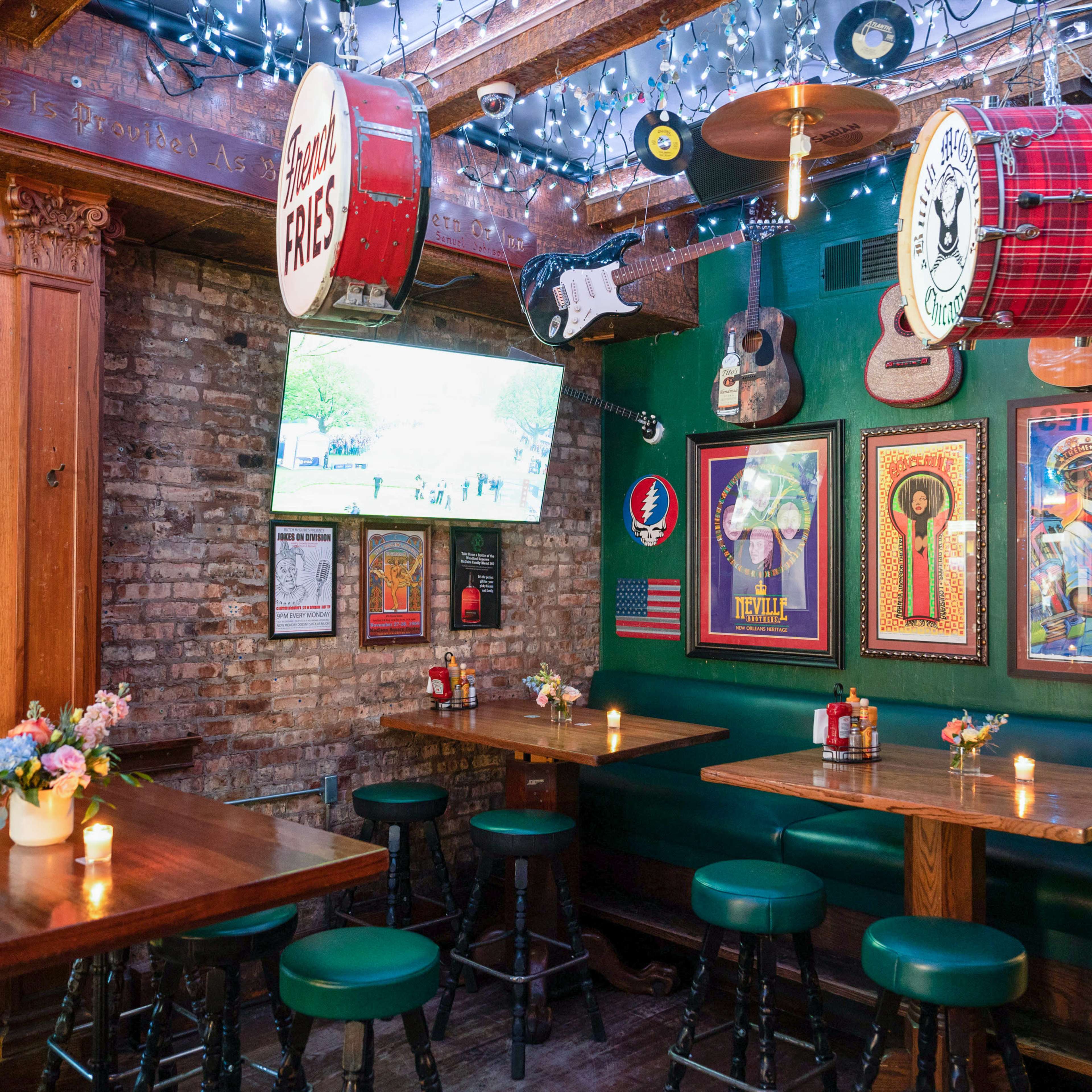 The interior of a bar features wooden tables, stools, and walls adorned with musical instruments and colorful artwork, illuminated by string lights.
