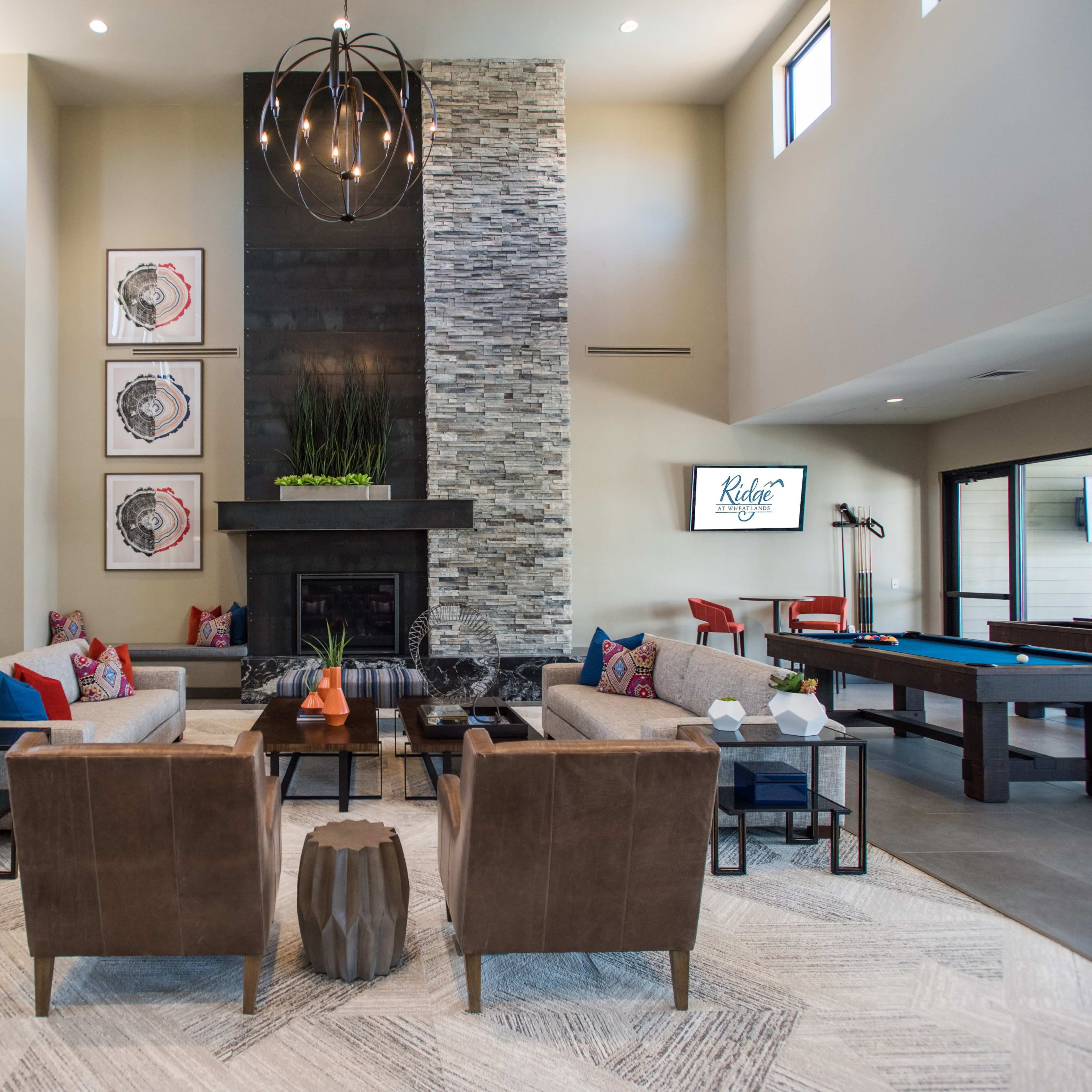 A modern living area with a stone fireplace, comfortable seating arrangements, and a large window-filled space.