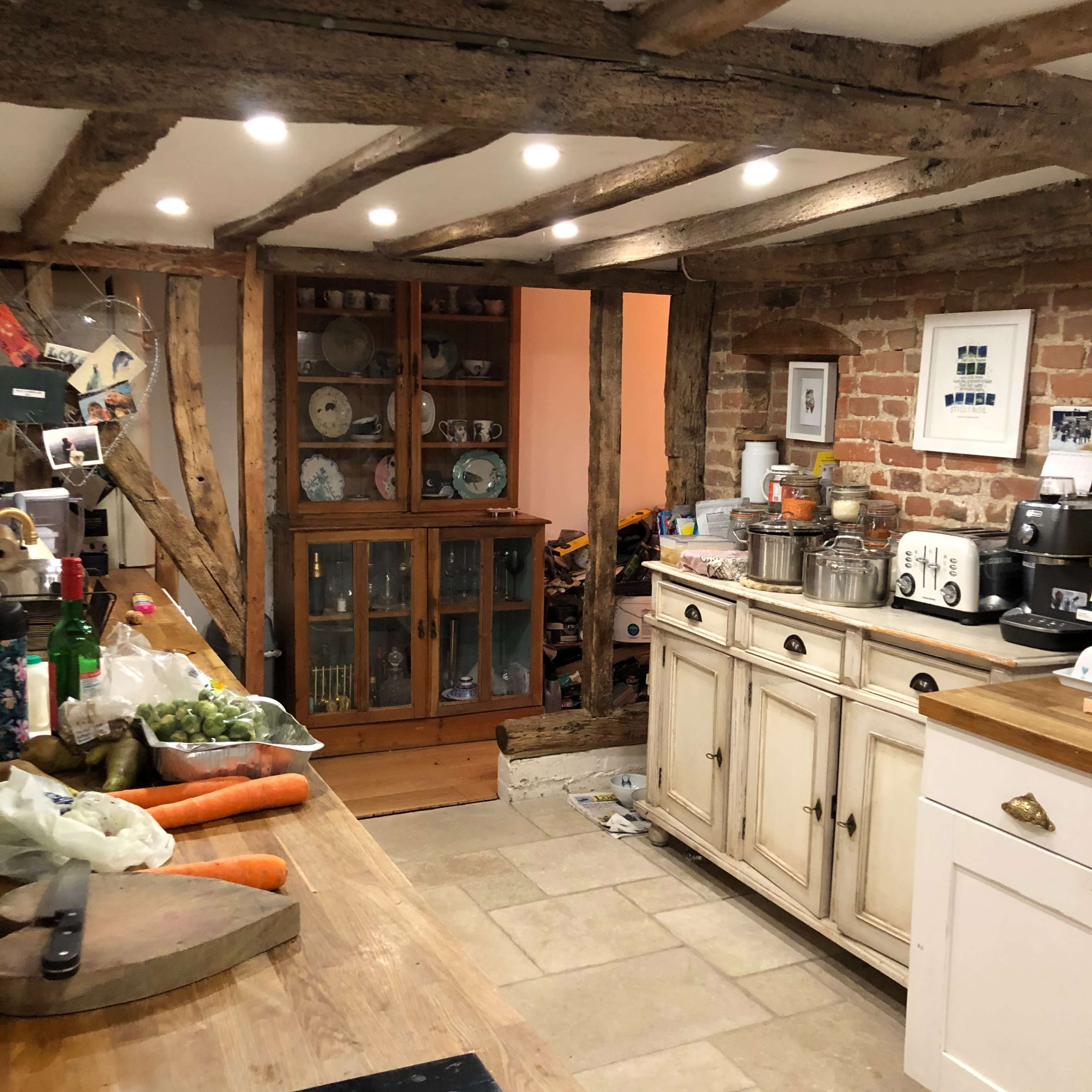 A rustic kitchen with wooden beams, a central island, and a glass-fronted cabinet displaying dishes.