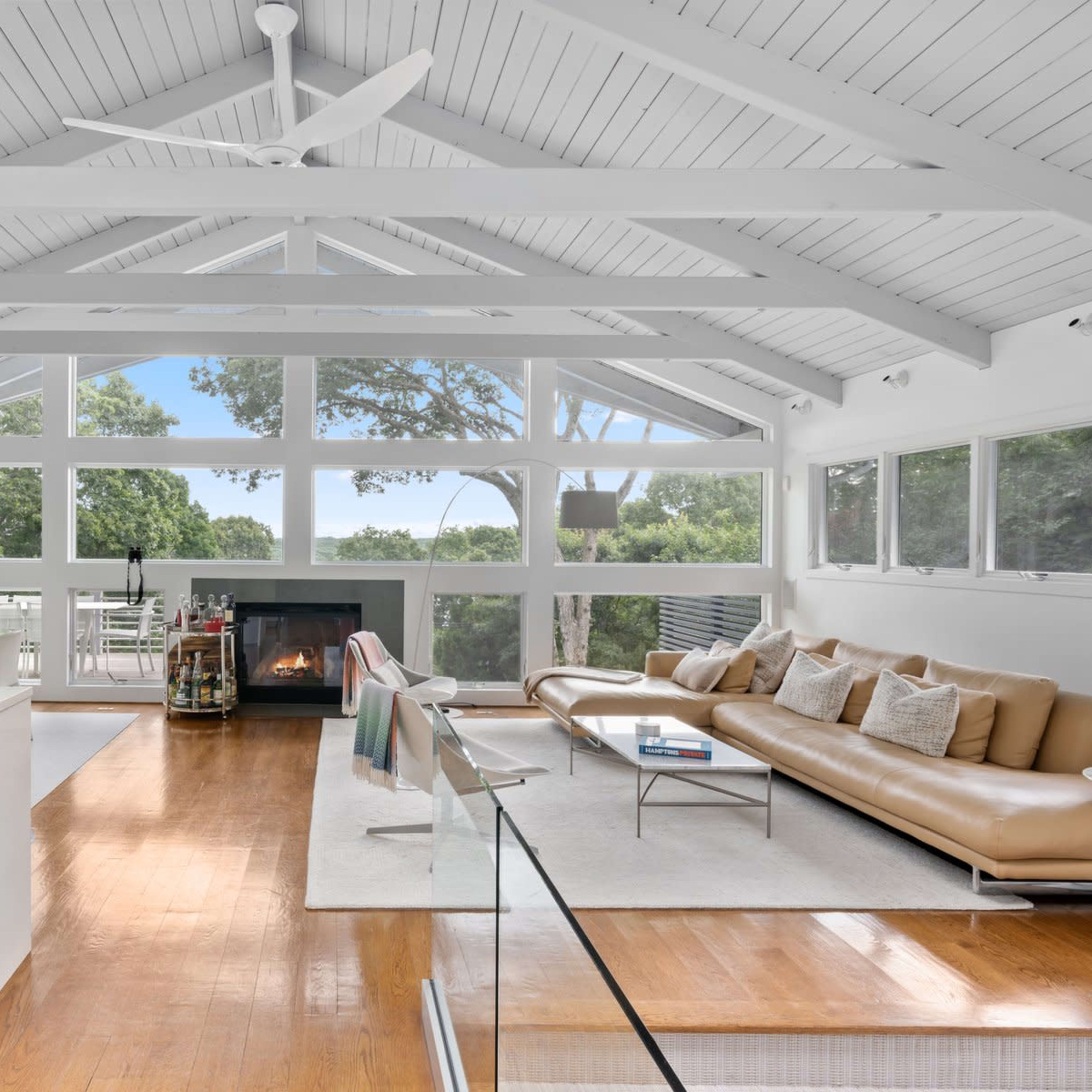 A modern living room with large windows, a fireplace, and a view of greenery outside.
