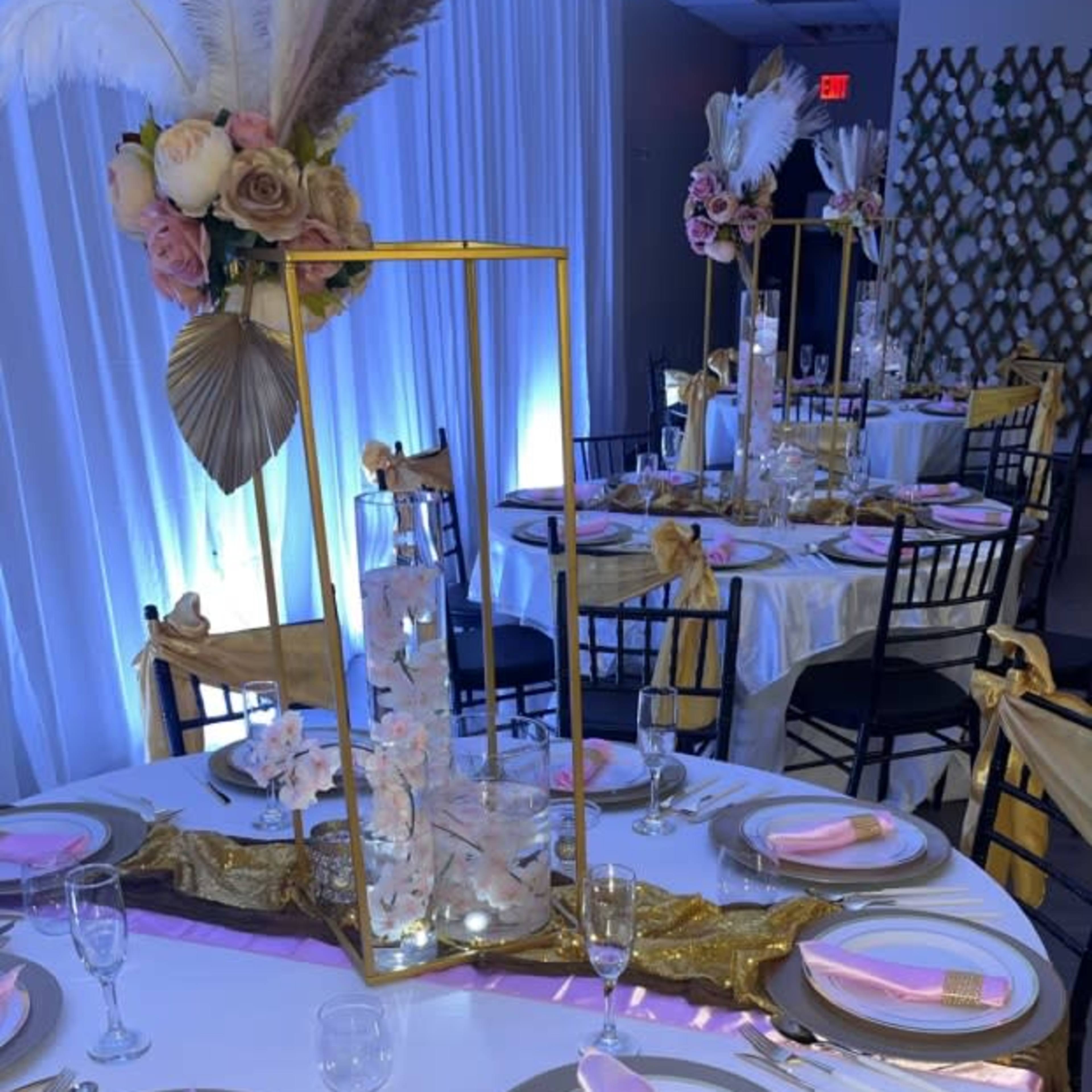 A elegantly arranged banquet table is set with gold and black chairs, featuring floral centerpieces and pink napkins.