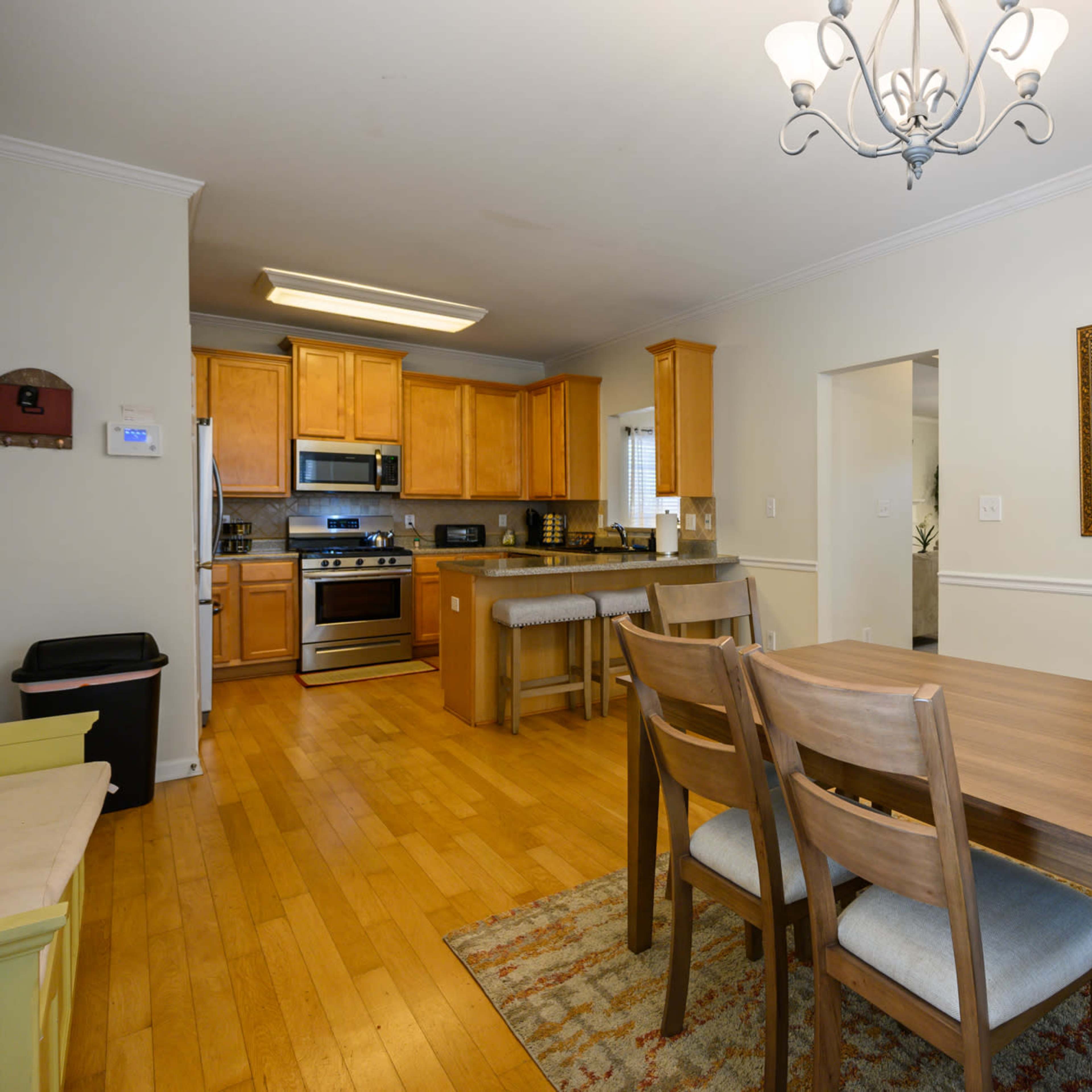 A dining area with a wooden table and chairs, adjacent to a kitchen featuring wooden cabinets and modern appliances.