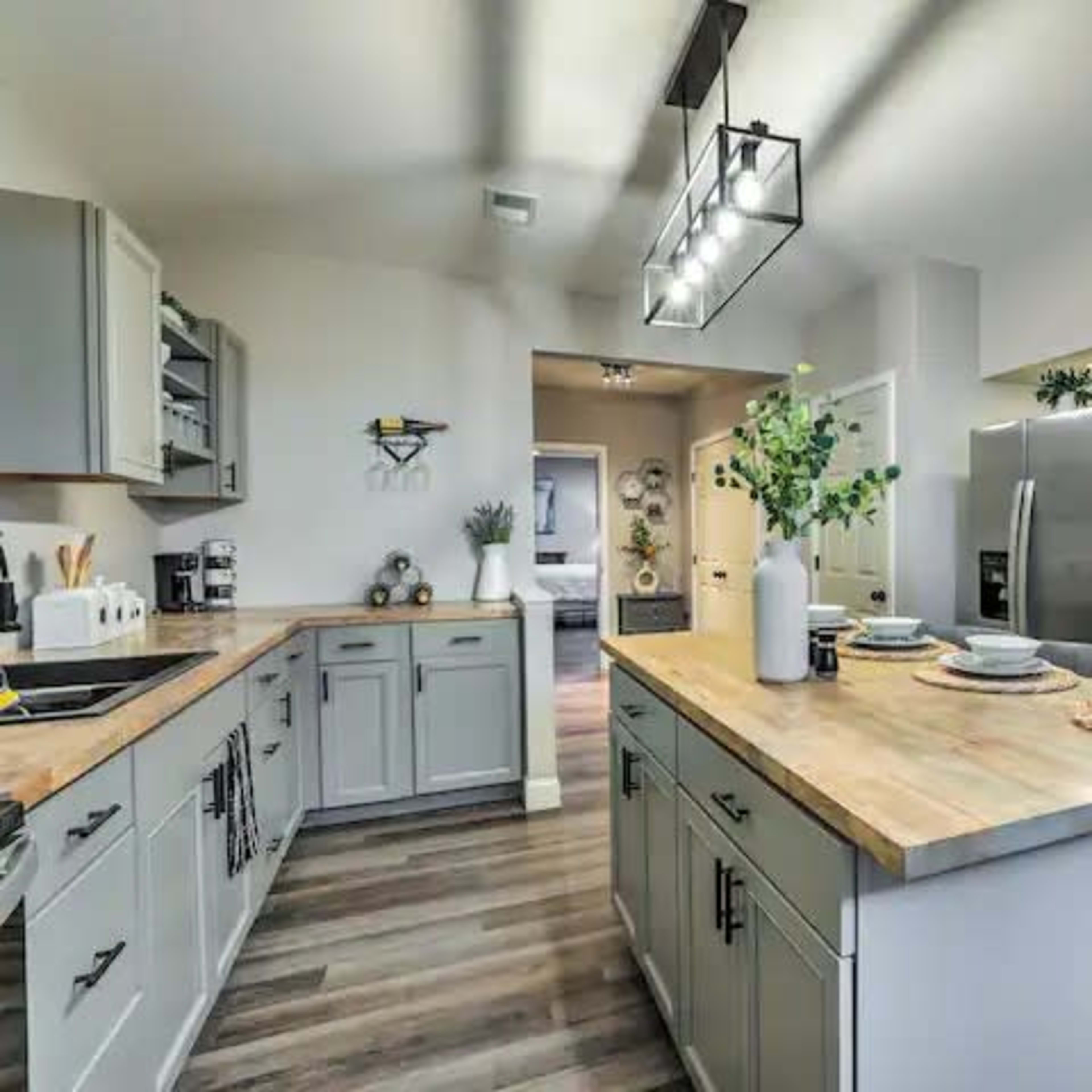 A modern kitchen with gray cabinetry, a central island with seating, and stainless steel appliances, all set against a backdrop of natural wood flooring.