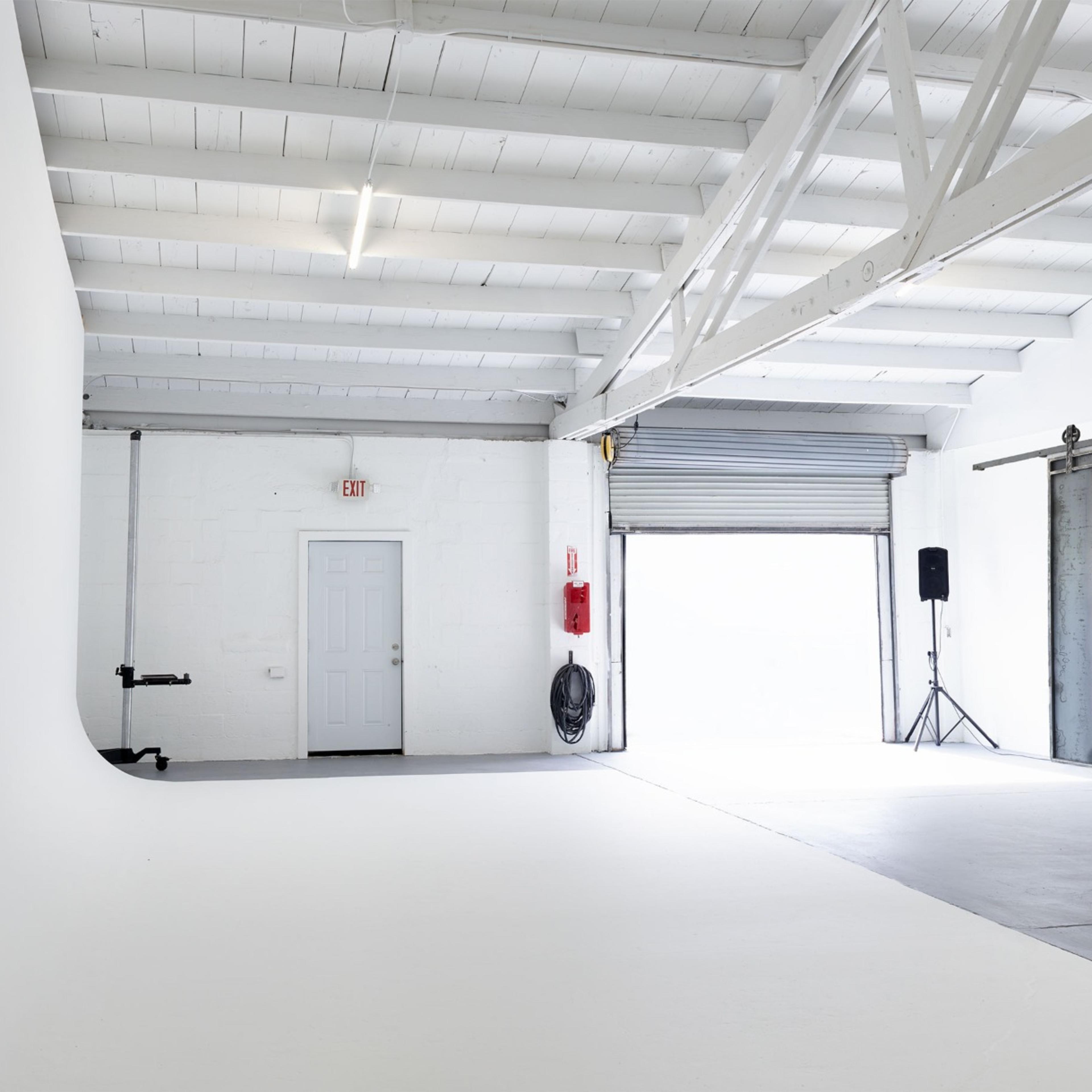 A spacious, empty studio with white walls, a concrete floor, and large industrial-style doors.
