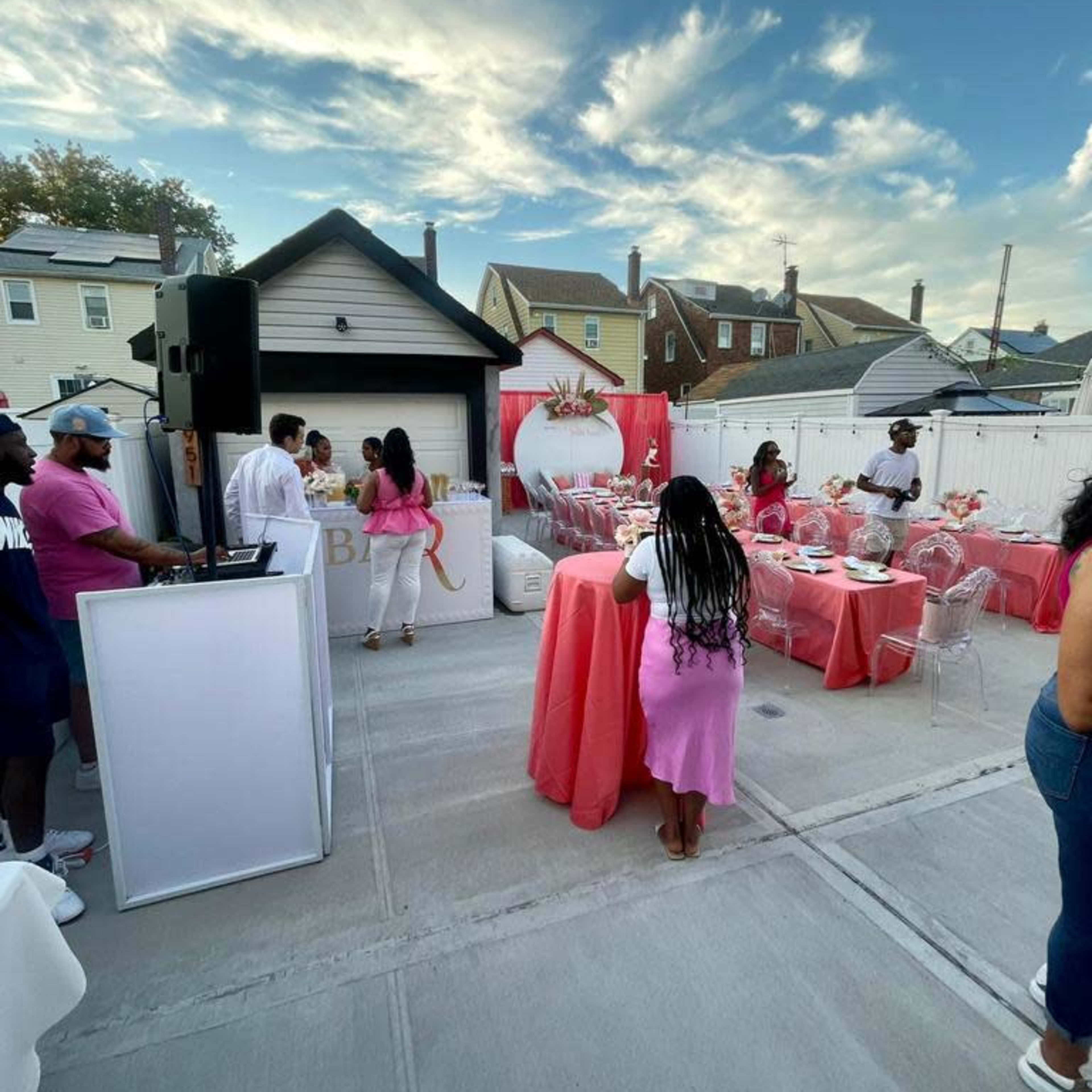 A gathering is taking place in an outdoor setting with pink decorations and guests socializing among tables.