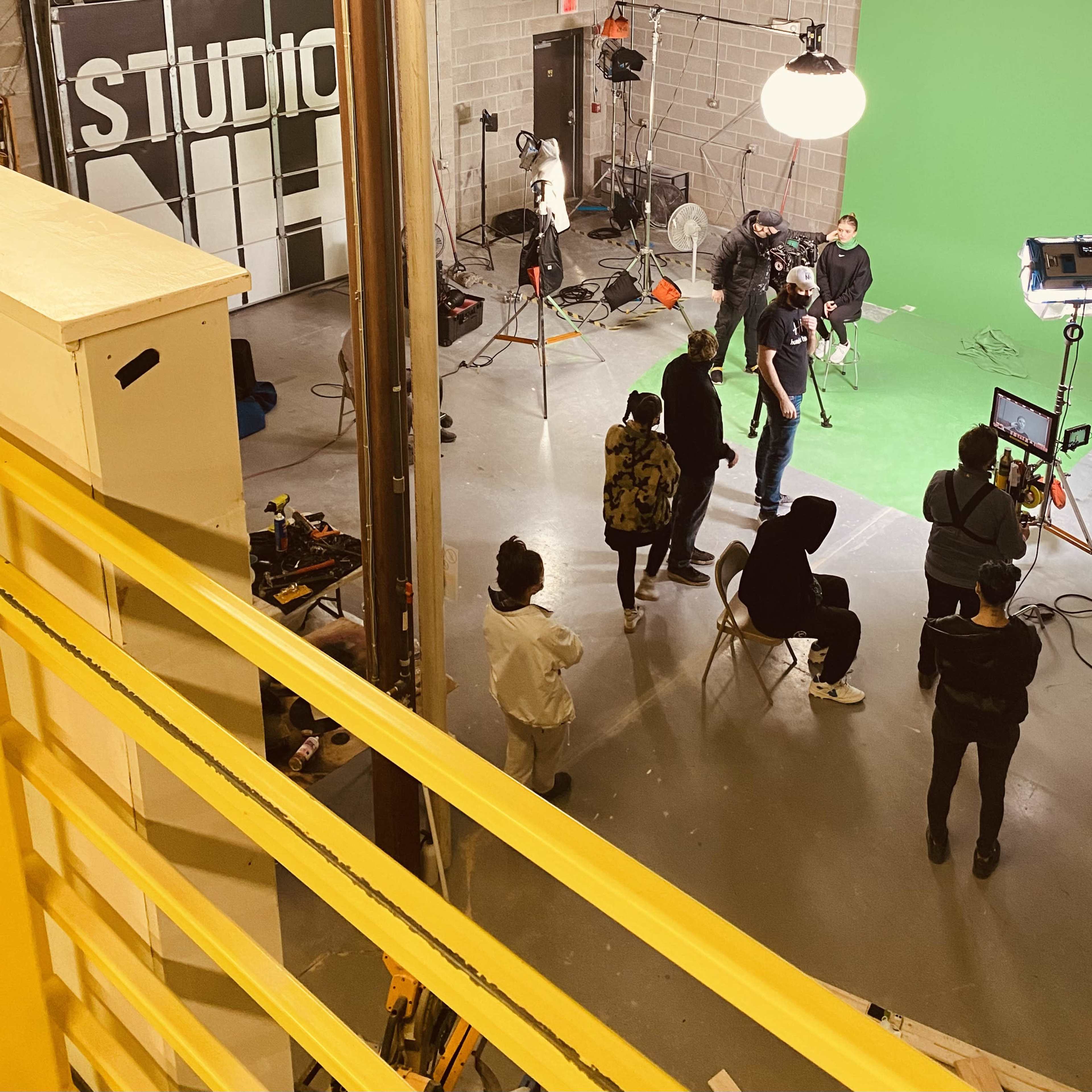 A film crew works in a studio setting with a green screen and various lighting equipment.