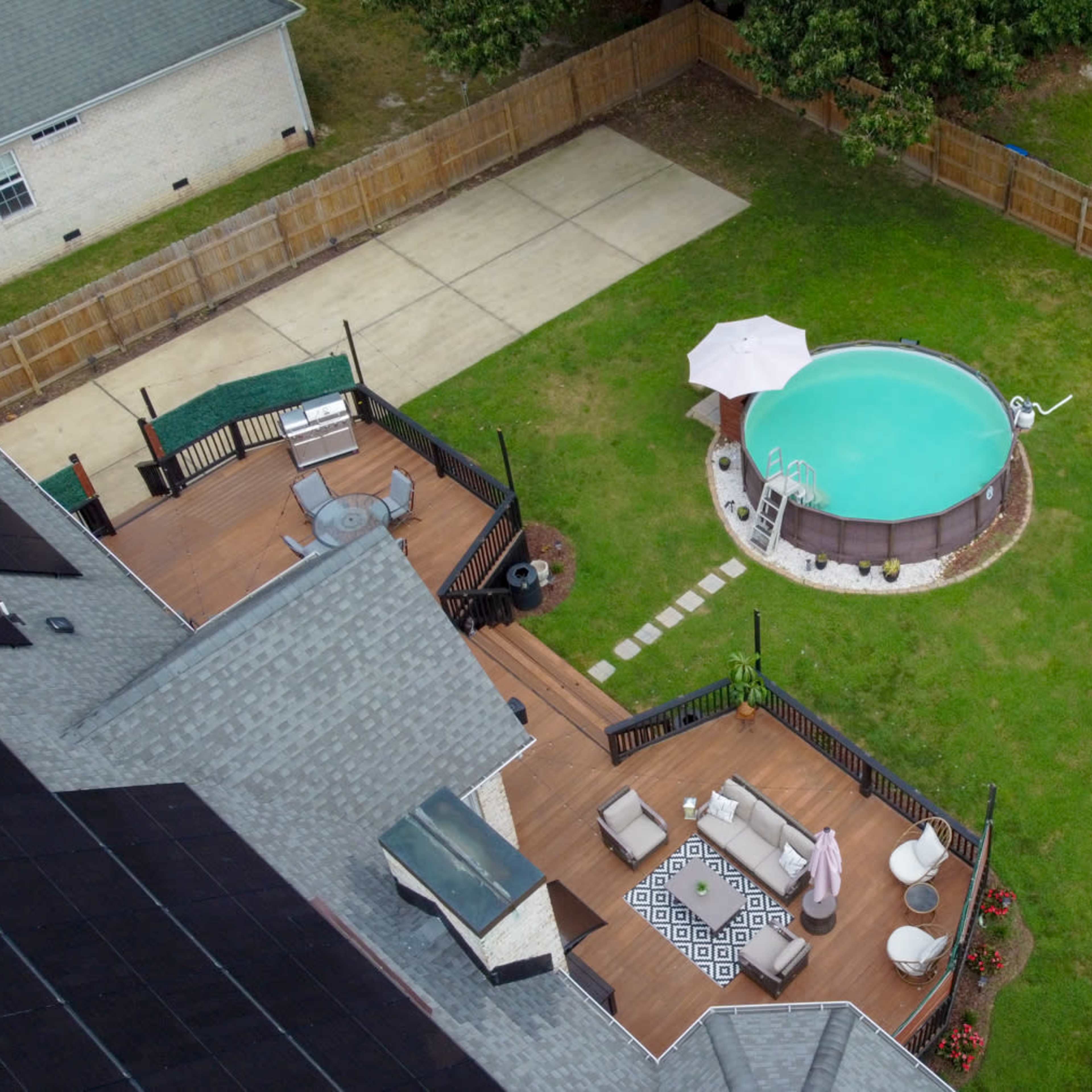 An aerial view shows a neatly landscaped backyard featuring a small pool, a patio area with seating, and a grassy lawn enclosed by wooden fencing.