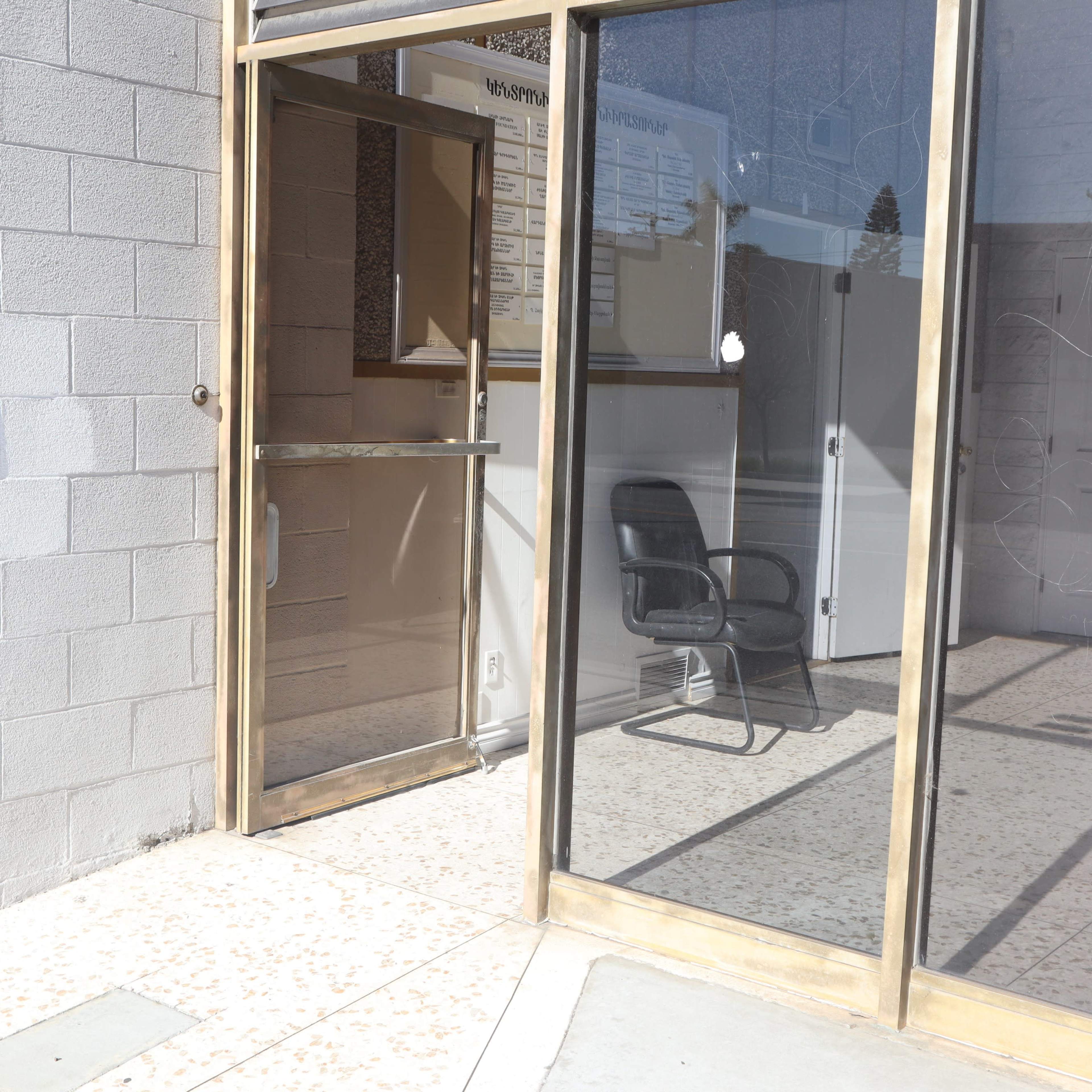 The entrance of a building with a glass door and a black chair visible inside.