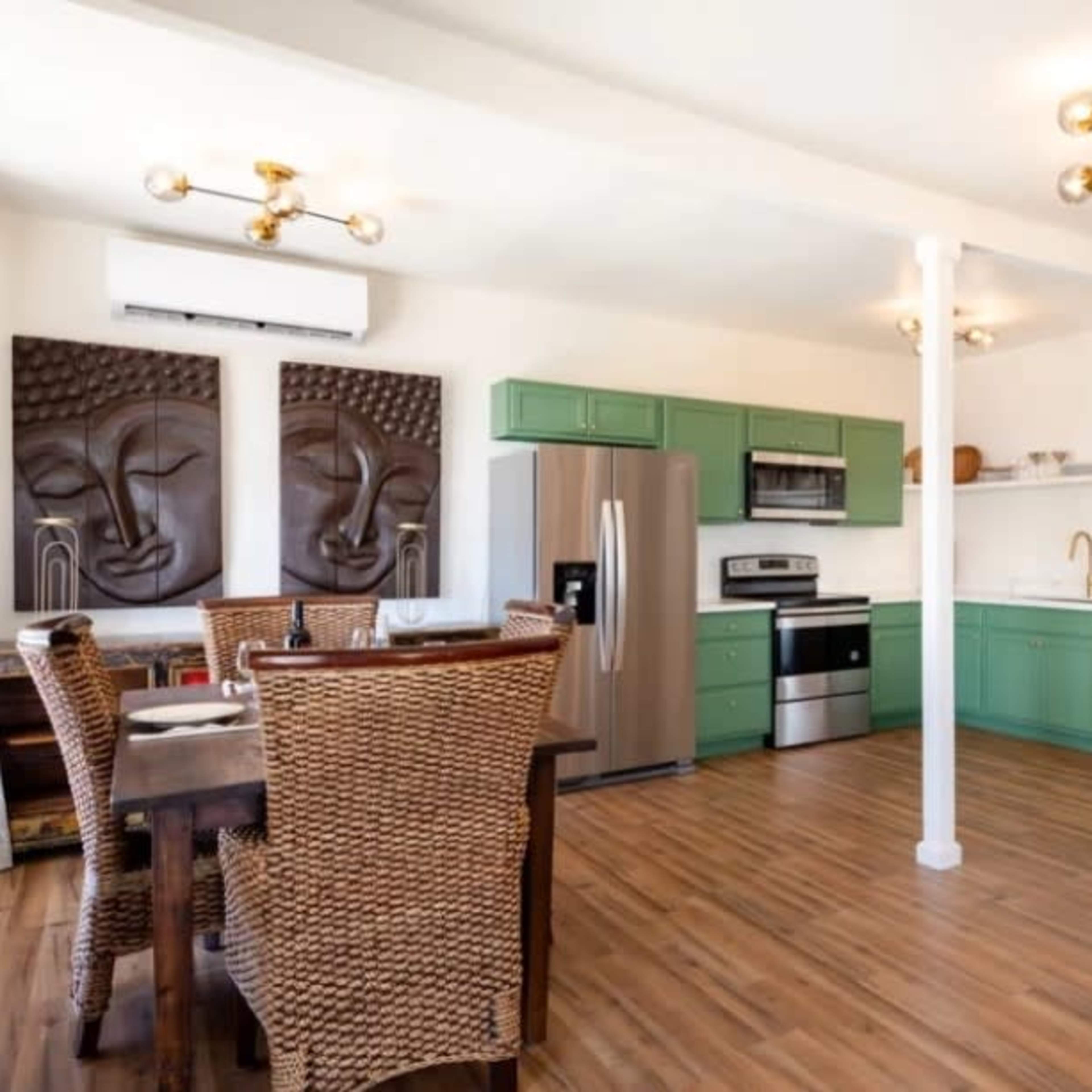 A modern kitchen and dining area with green cabinetry, stainless steel appliances, a wooden dining table, and artistic wall decorations.