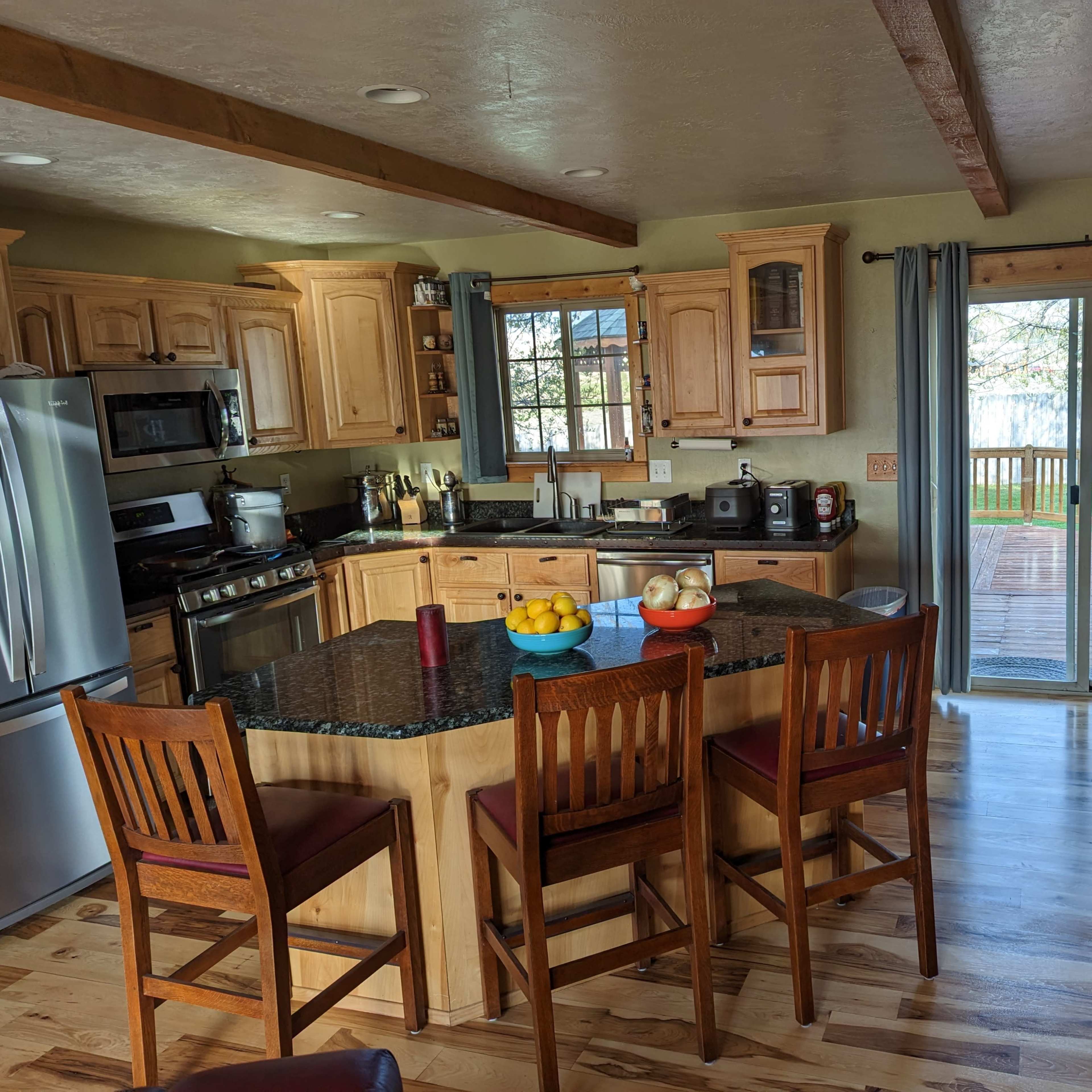 A spacious kitchen features wooden cabinets, a large island with seating for four, and sliding glass doors that lead to an outdoor deck.