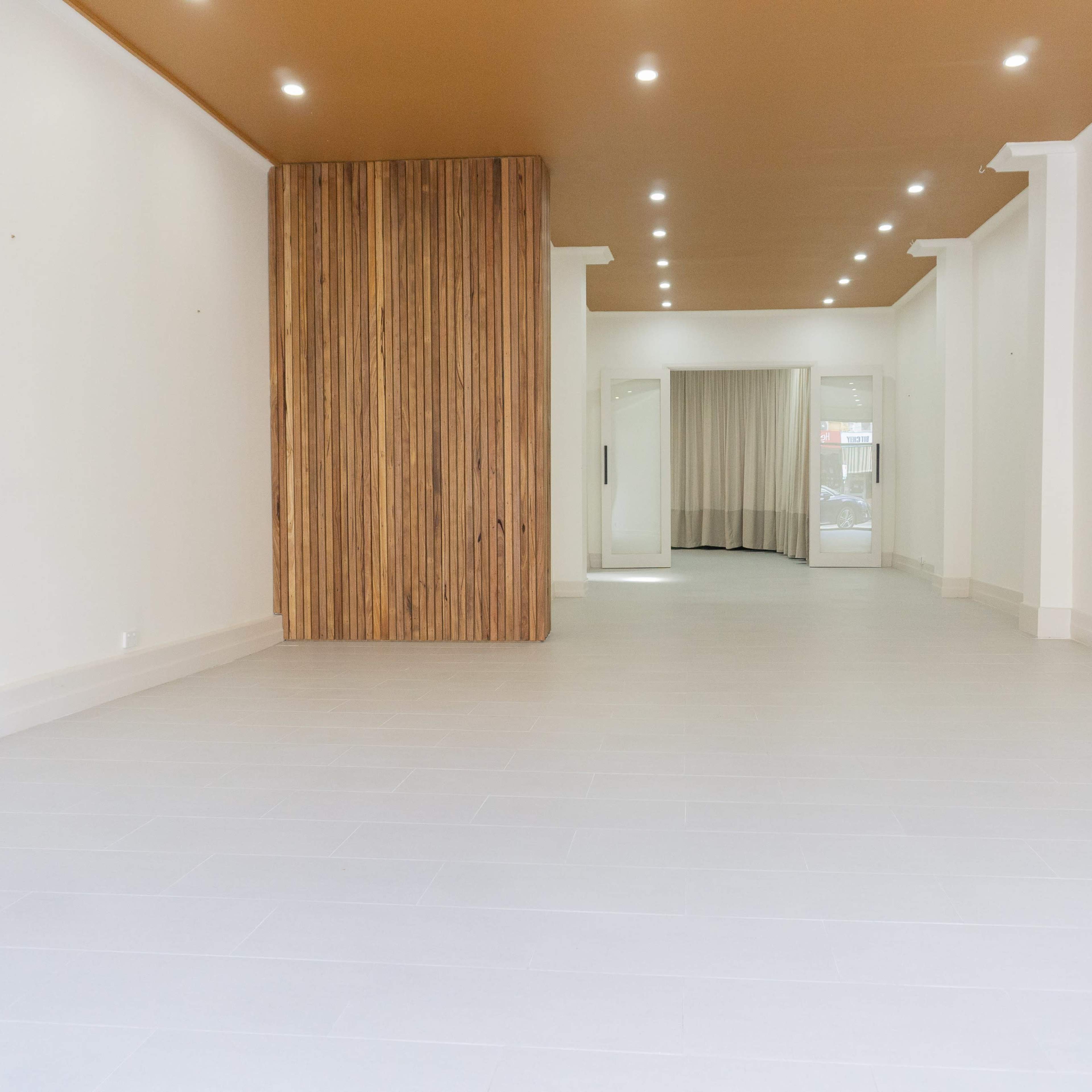 An empty room features a wooden accent wall, flat white walls, and a bright floor with ceiling lights illuminating the space.