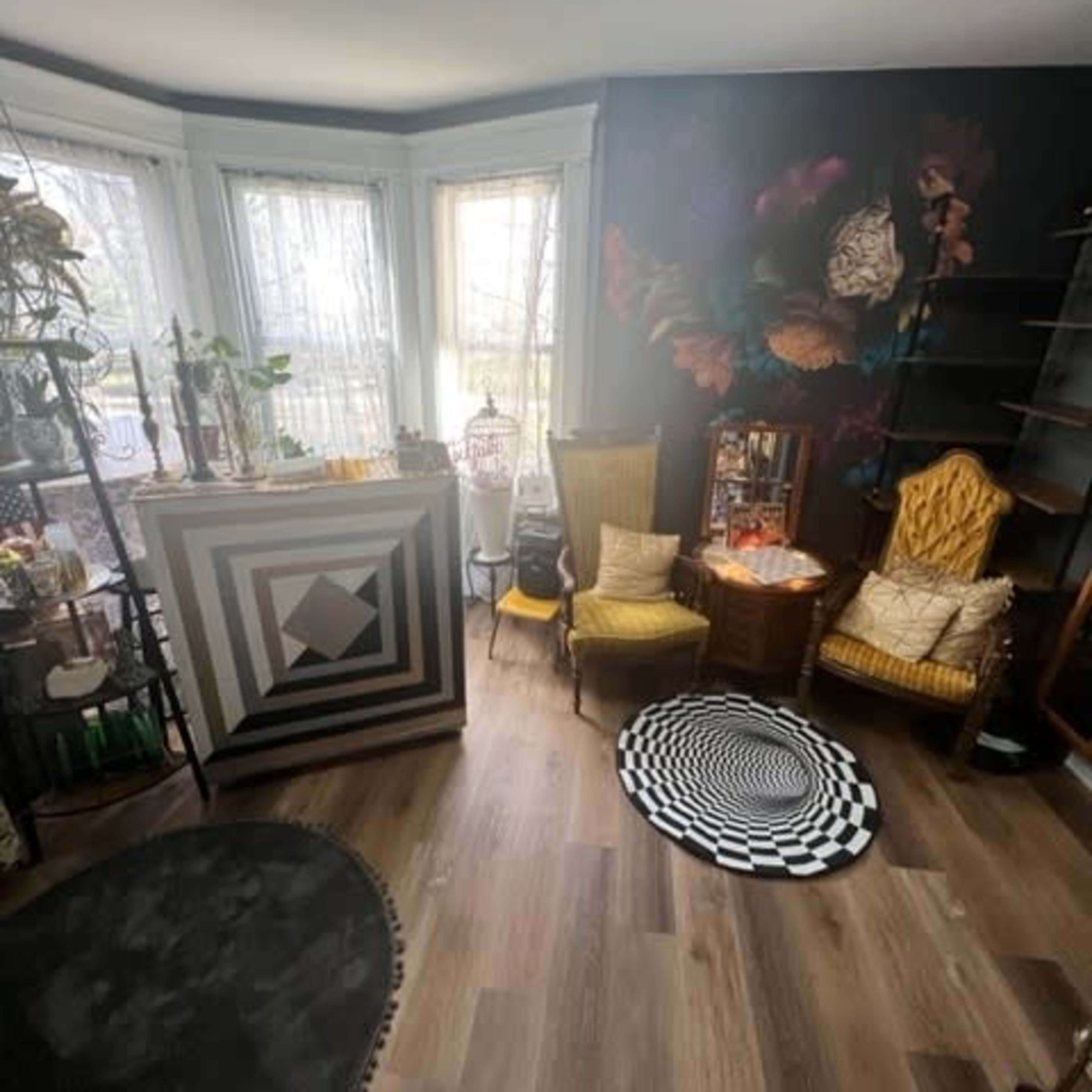 A room with a geometric-patterned bar area, two vintage chairs, a round patterned rug, and large windows allowing natural light.